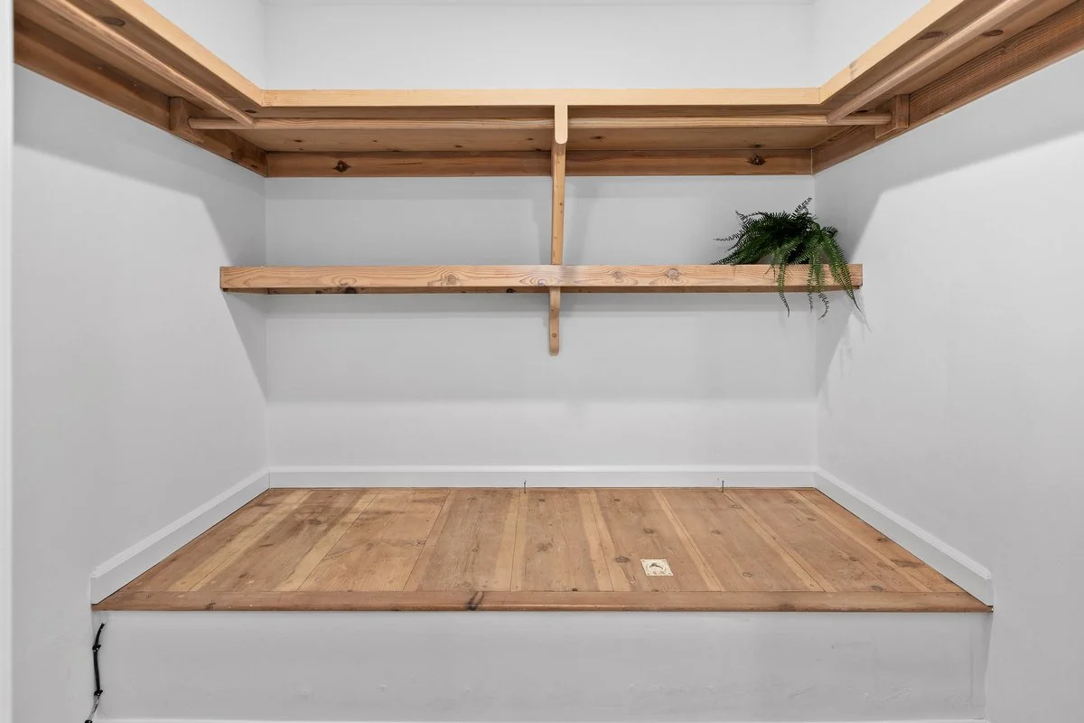 Empty closet with wooden shelves and a rustic wooden floor, with a potted fern on the right shelf.