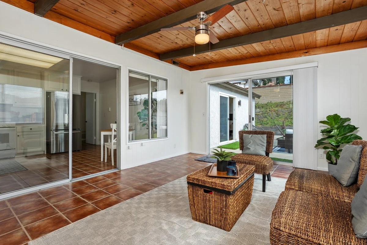 Living room with wicker chairs, a wicker coffee table, potted plants, a ceiling fan, and sliding glass doors leading outside.