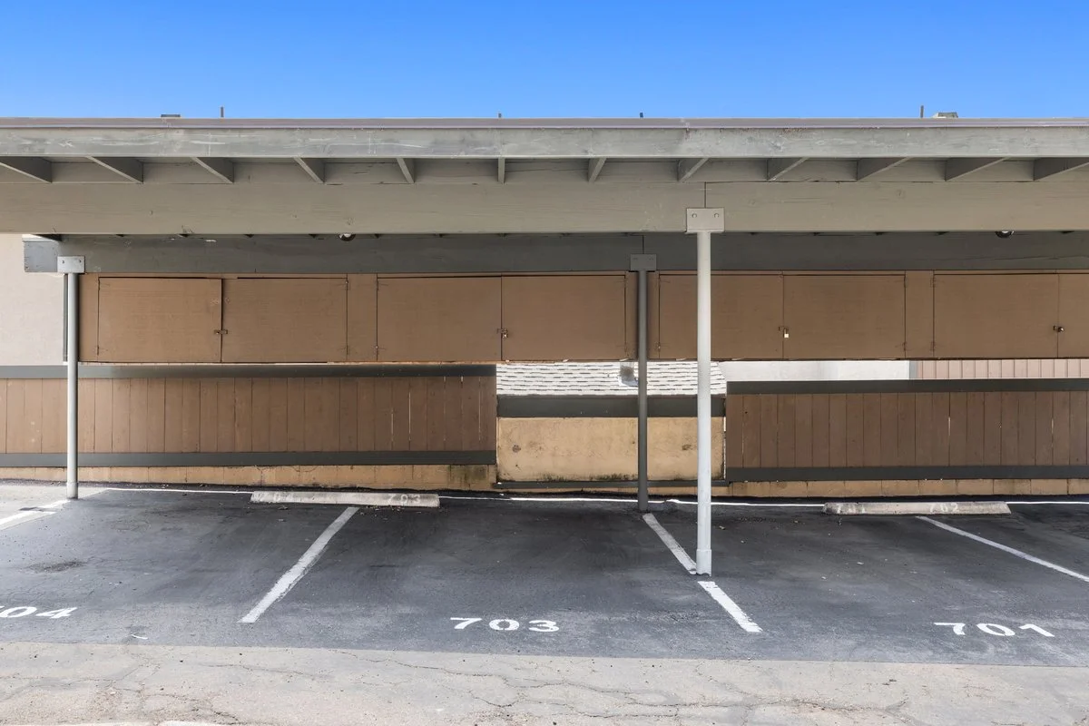 Empty parking lot with designated parking spaces numbered 701, 703, and 704, with a wooden guardrail and a building structure above.