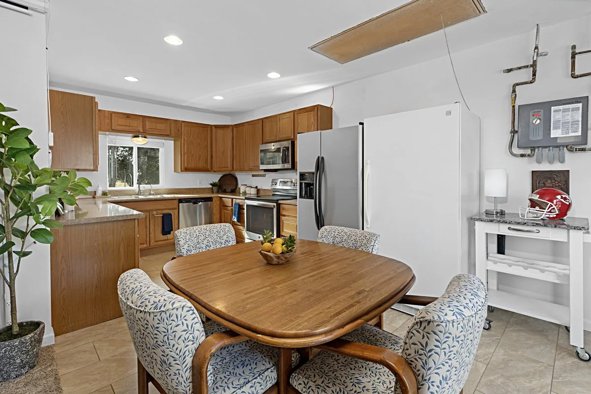 Kitchen with wooden cabinets, stainless steel appliances, a wooden dining table with four patterned chairs, and a bowl of lemons on the table.
