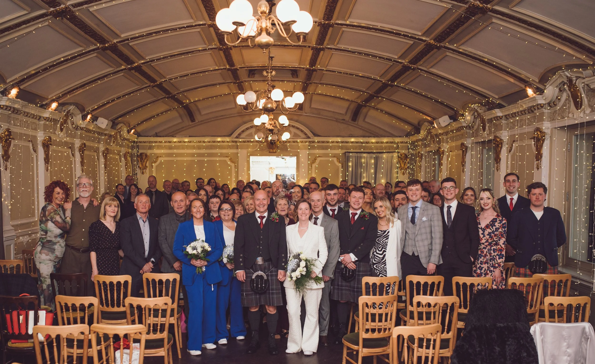Newlywed couple surrounded by family and friends in a joyful wedding group photograph