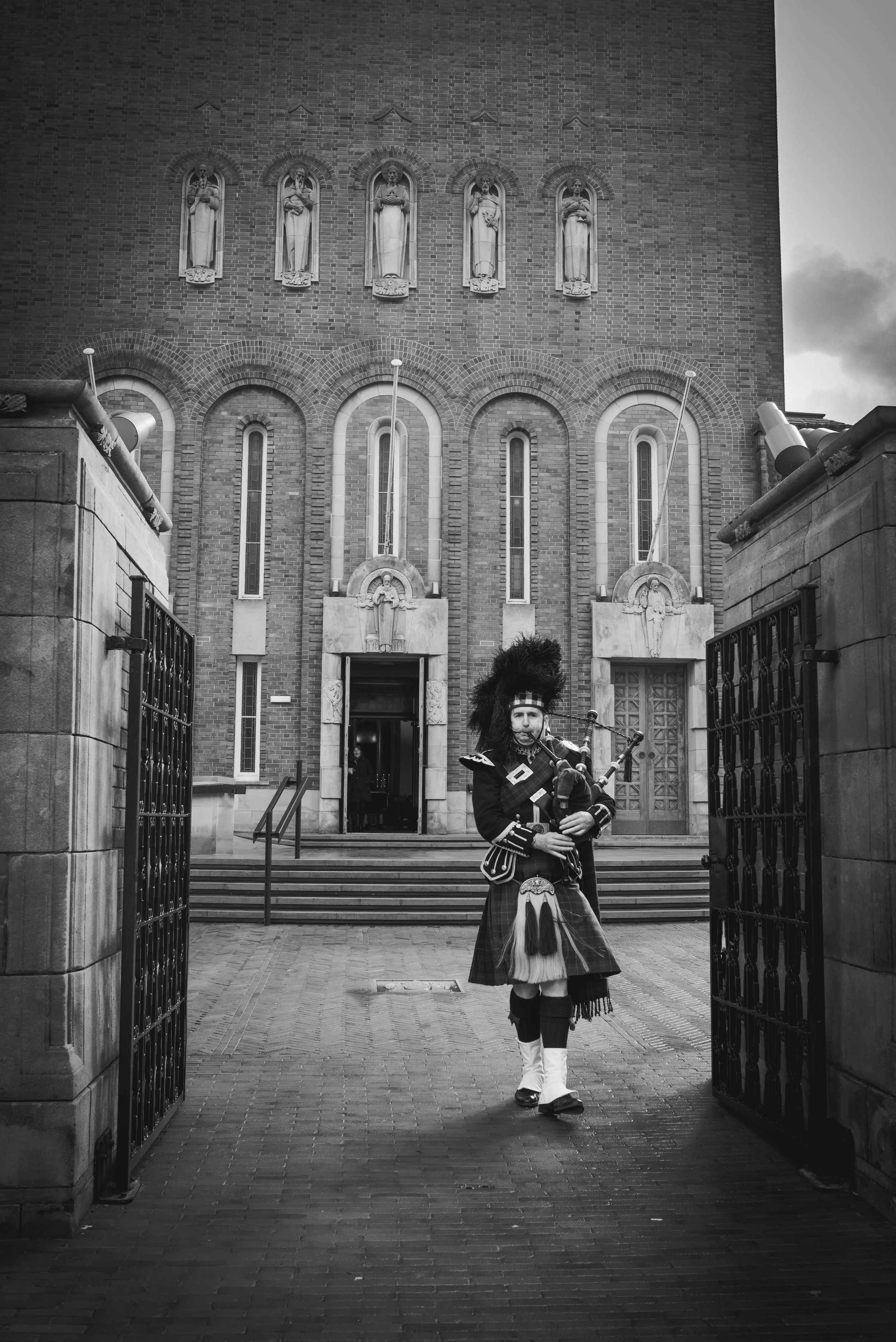 Scottish piper walking through the gates outside a wedding ceremony