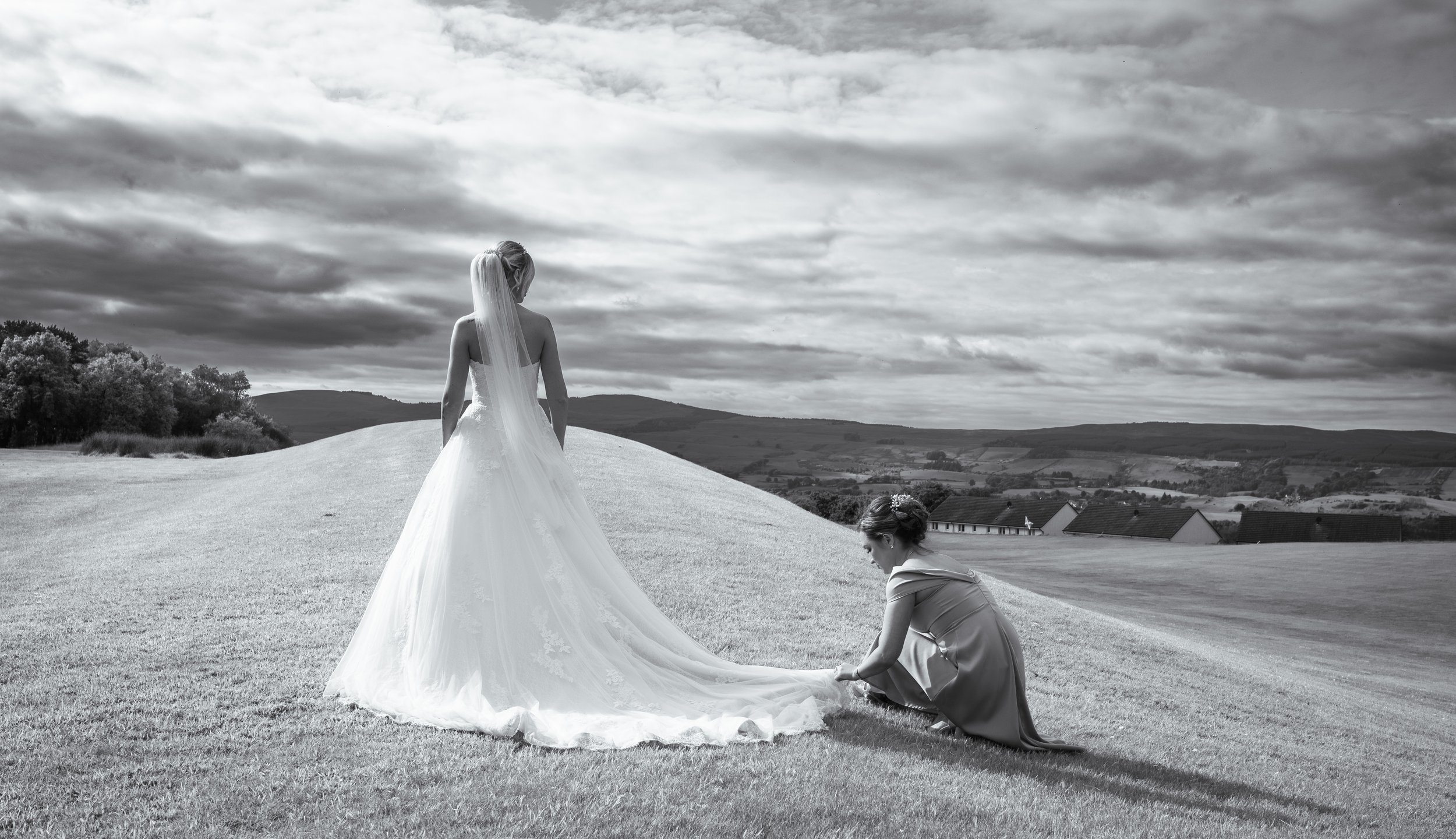 Bride and bridesmaid adjusting the wedding dress outdoors during portraits