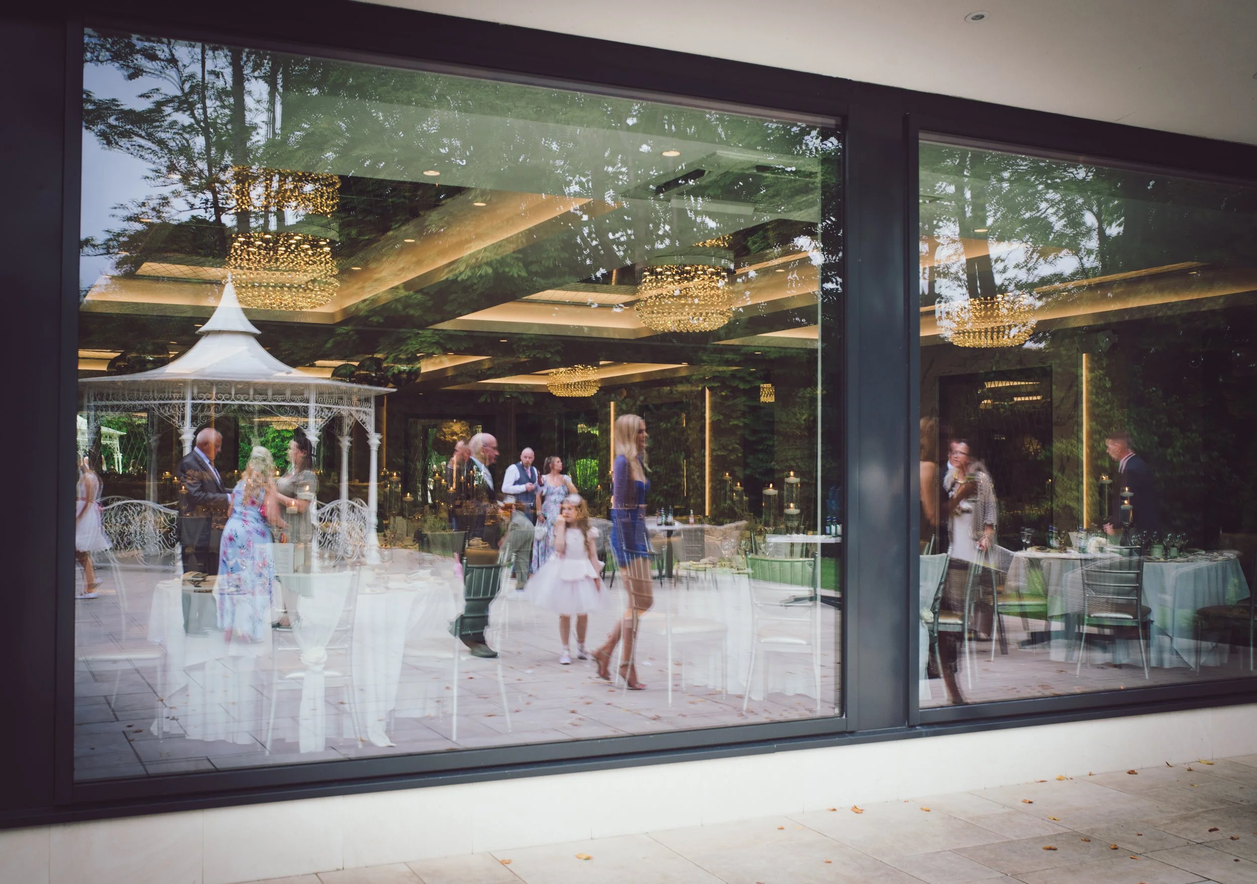 Wedding reception captured through the venue windows with guests enjoying the celebrations