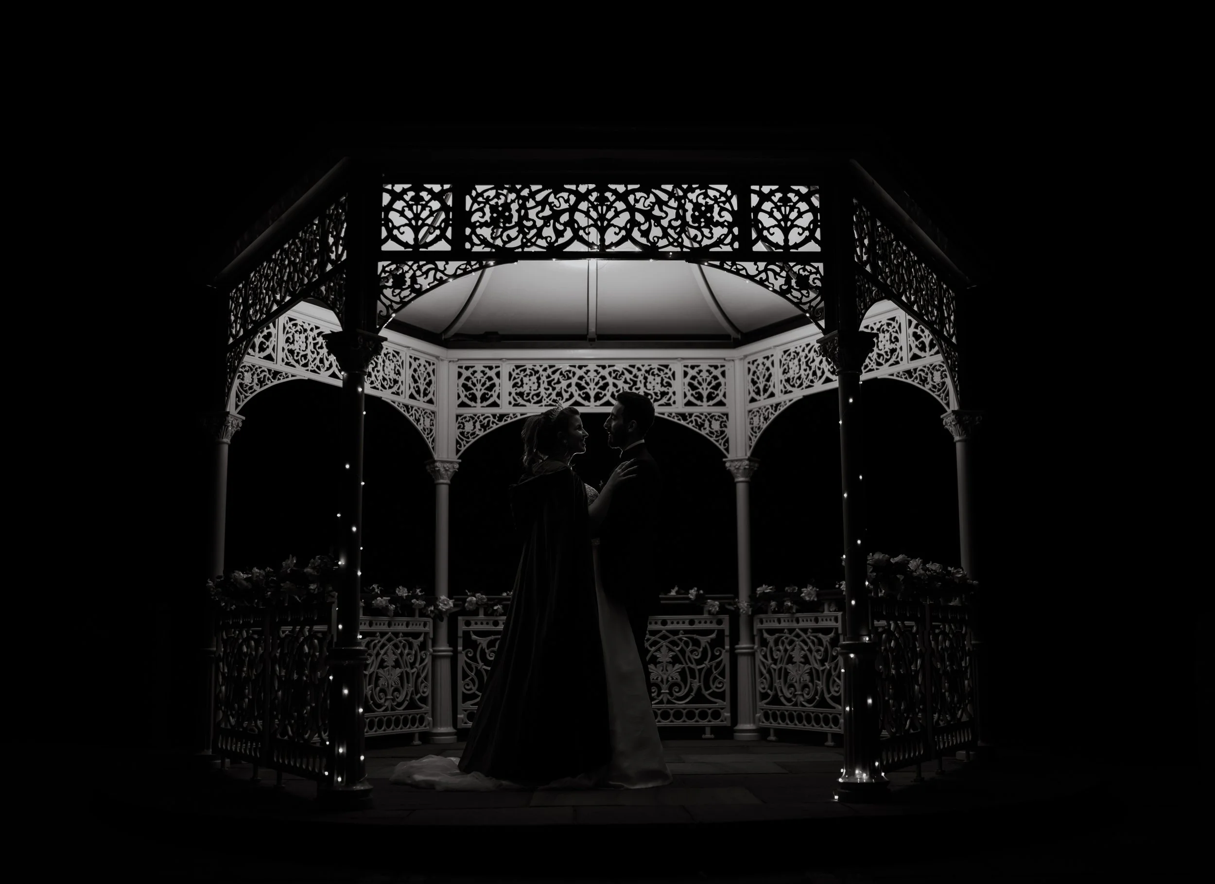 Bride and groom sharing an intimate moment beneath an illuminated gazebo during their evening reception