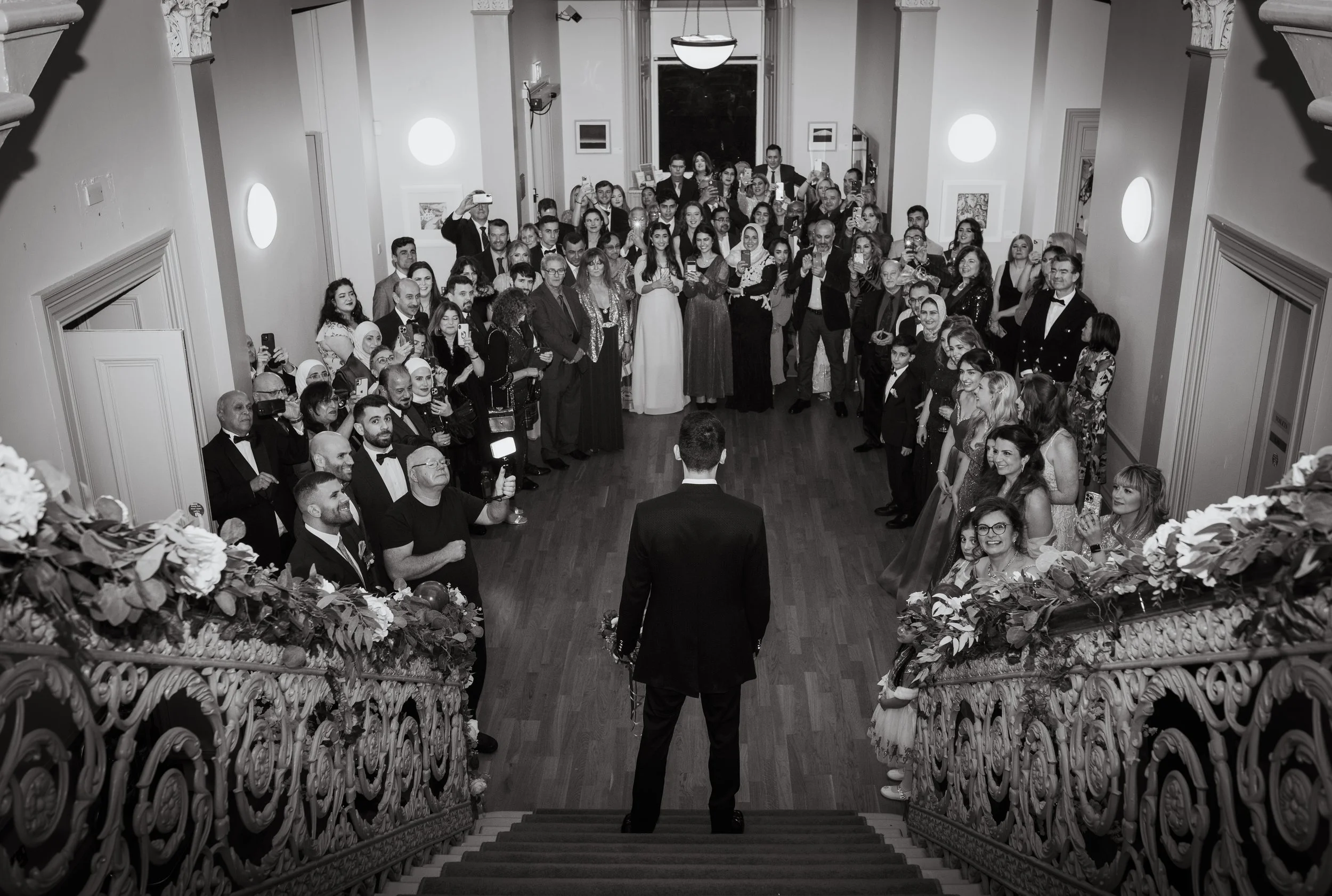 Groom looking towards wedding guests from a staircase