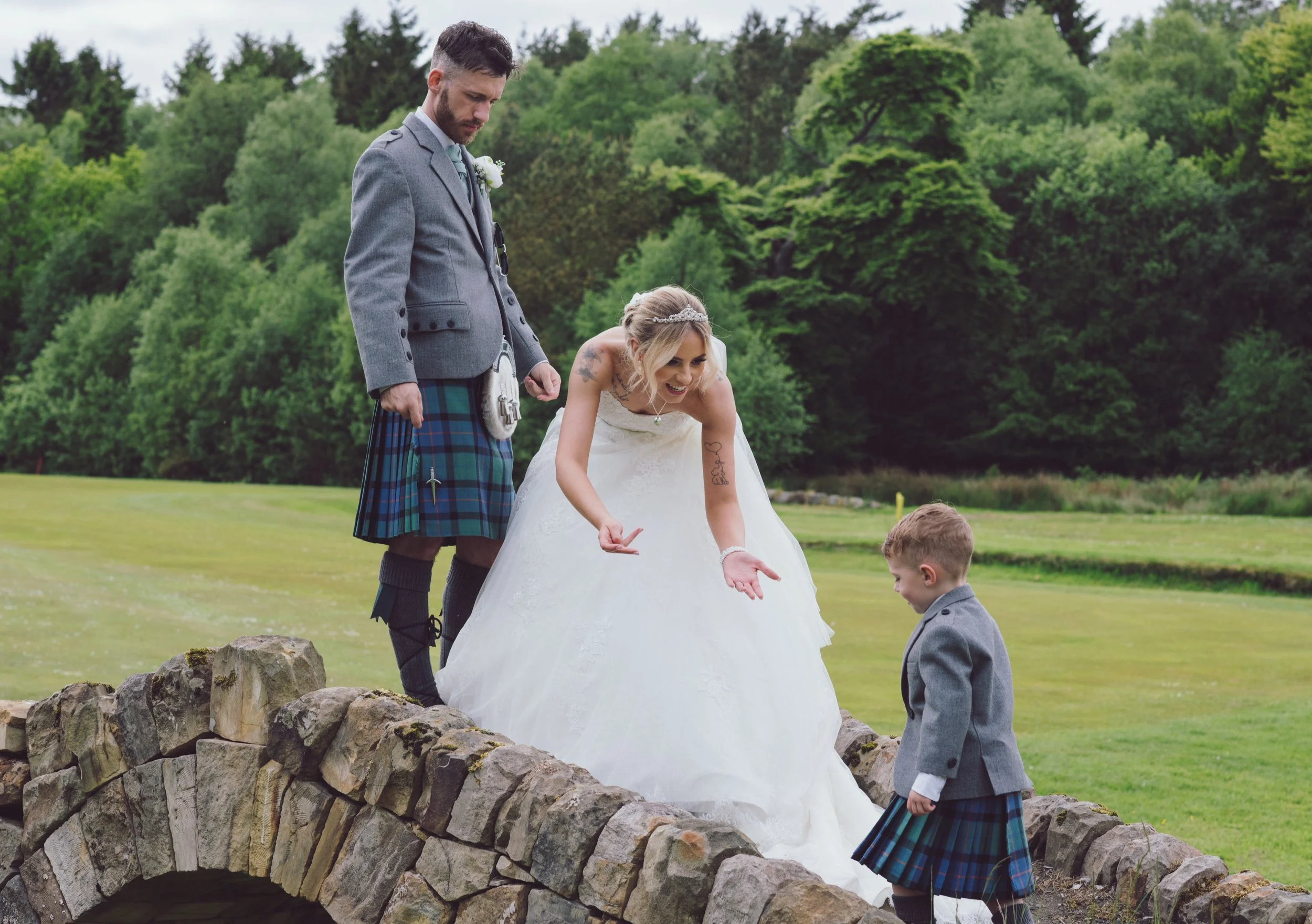 Bride laughing with a young page boy beside her groom on the stone bridge
