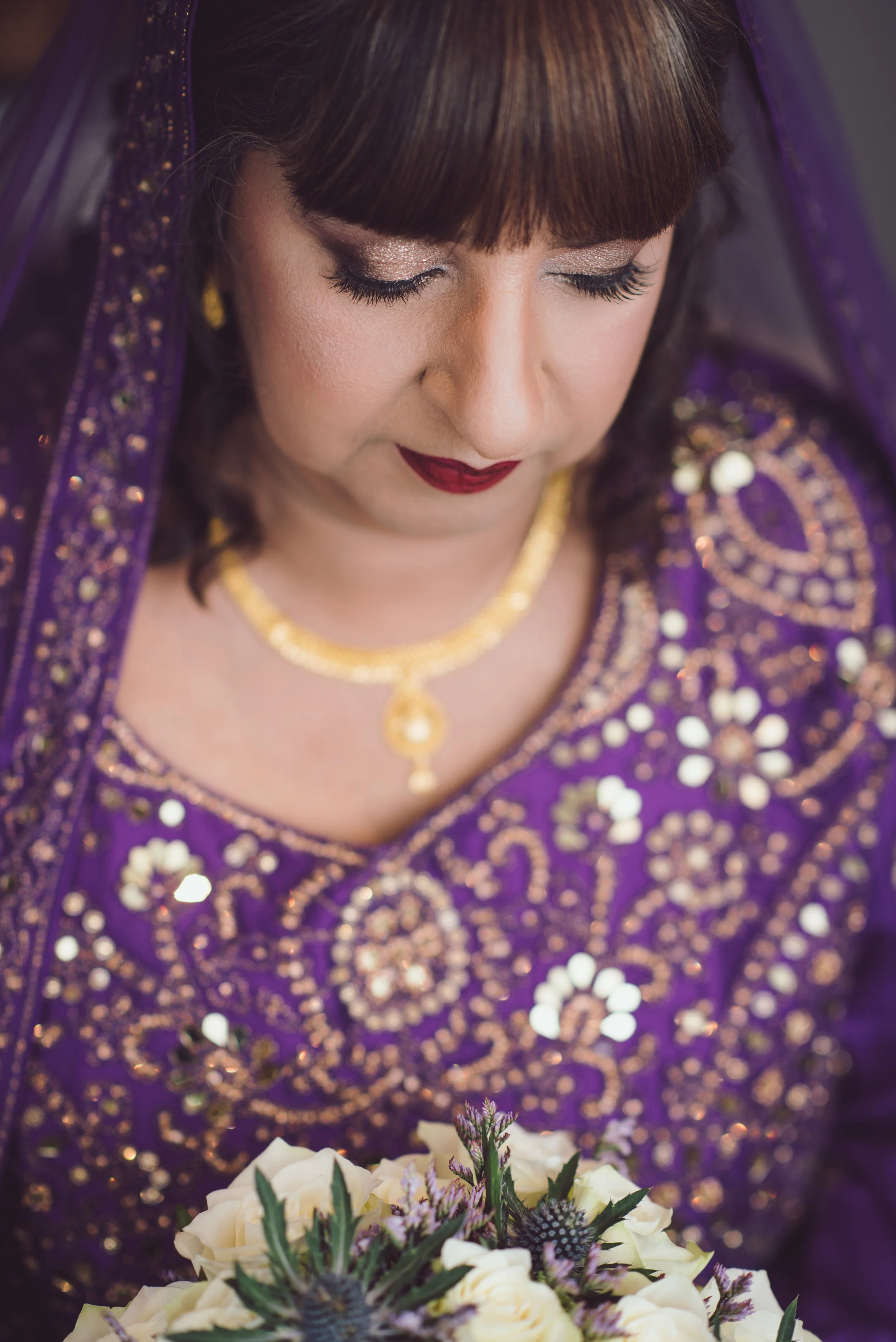 South Asian bride in a beautiful purple and gold wedding outfit holding her bouquet
