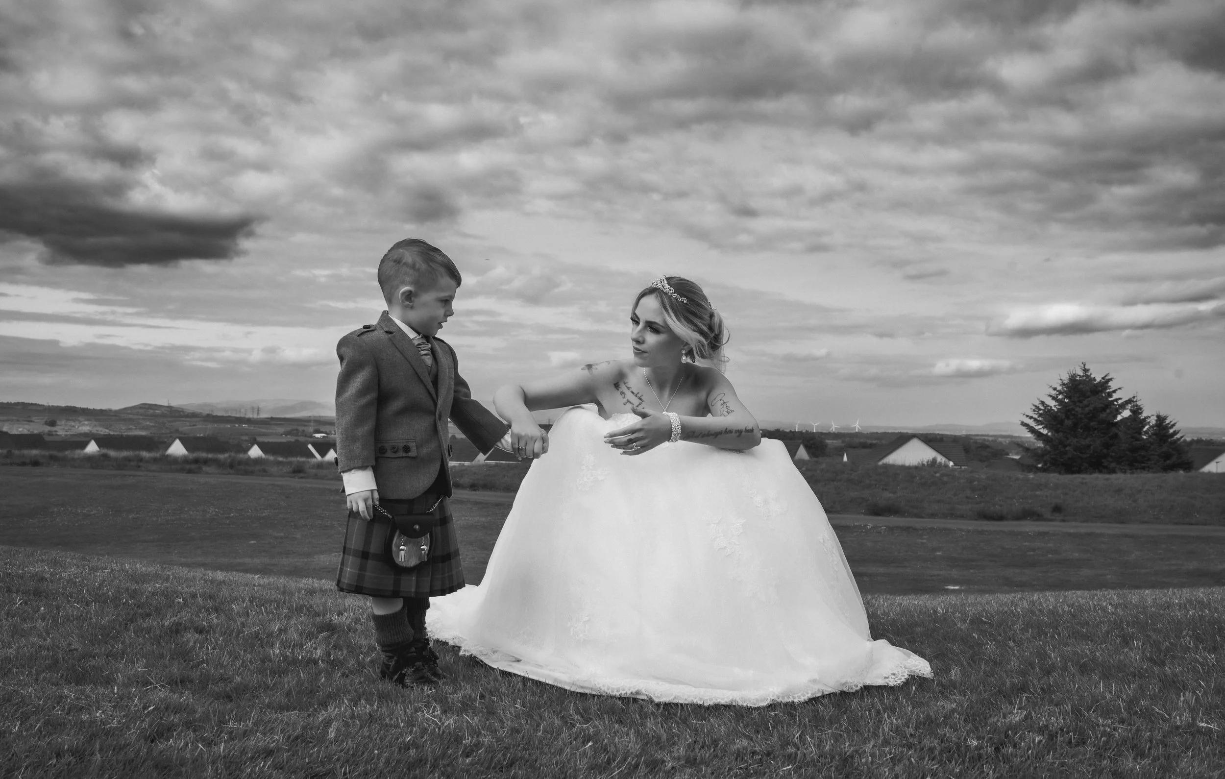 Bride sharing a quiet moment with a young page boy outdoors on her wedding day