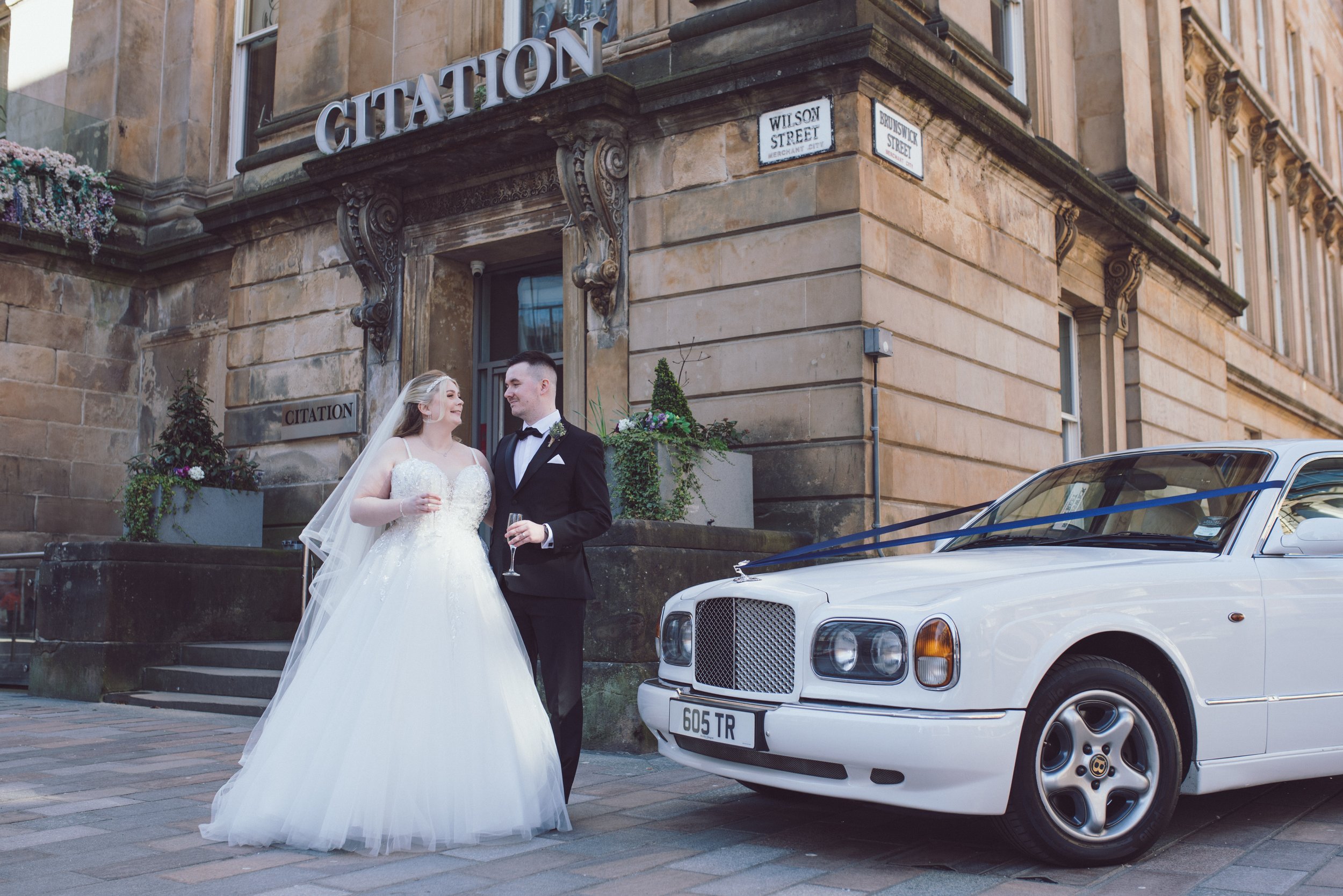 Bride and groom standing outside Citation with their classic wedding car in Glasgow