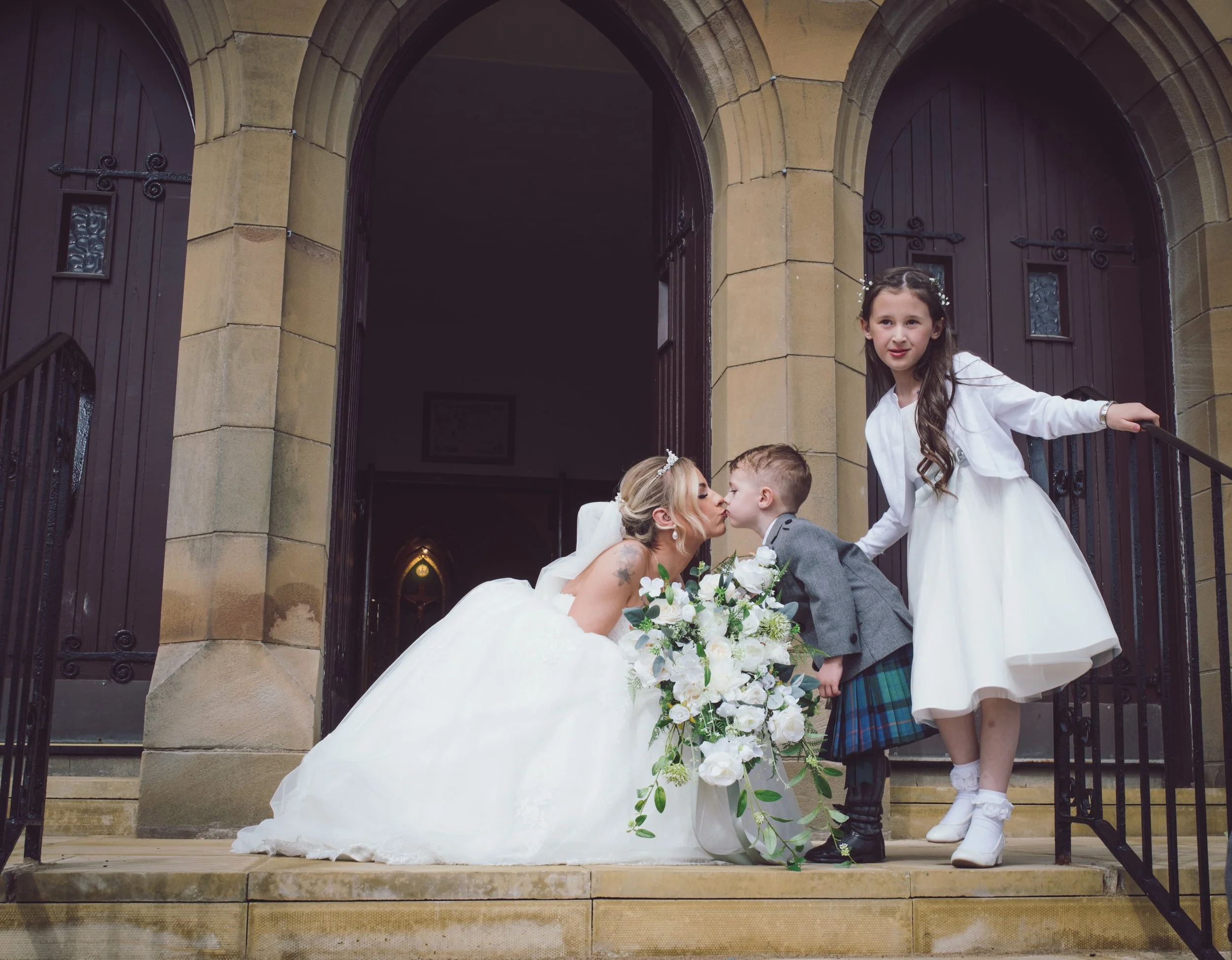 Bride kissing a young page boy outside the church on her wedding day