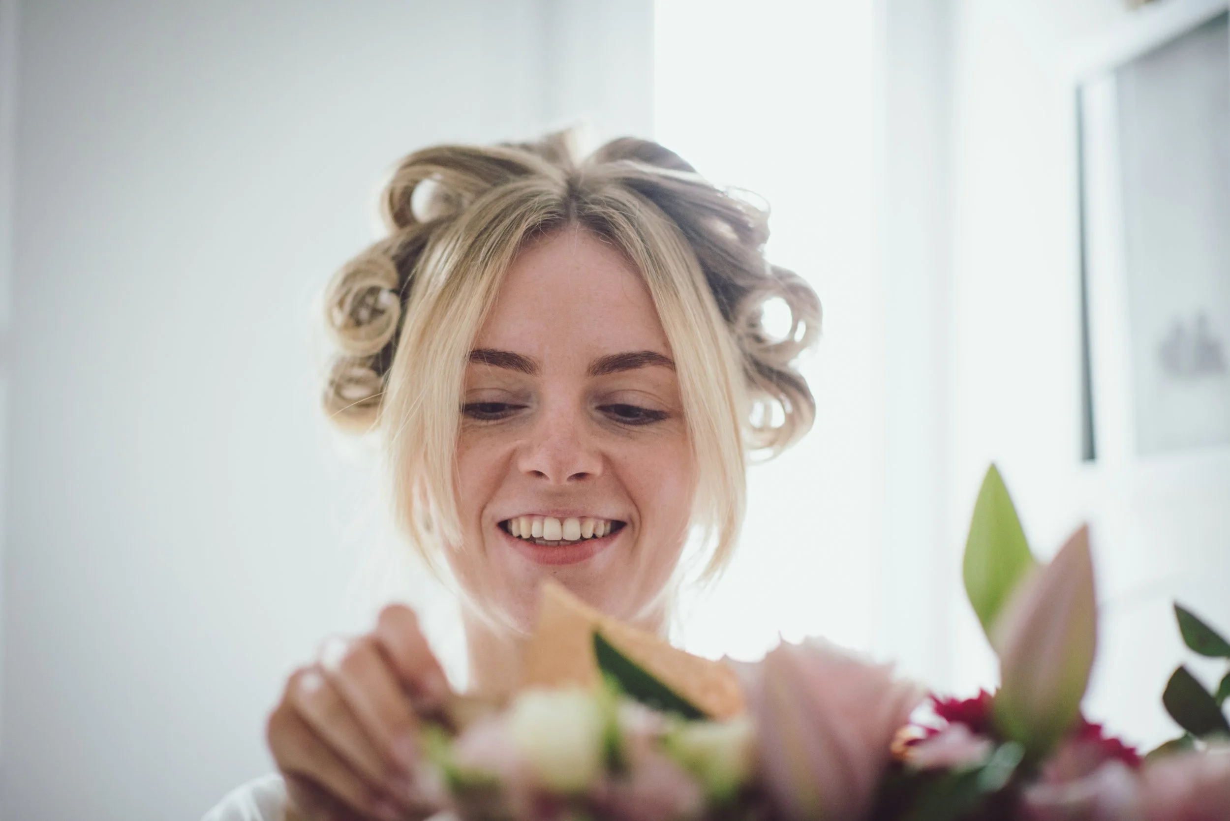 Bride smiling as she looks at her wedding bouquet during preparations