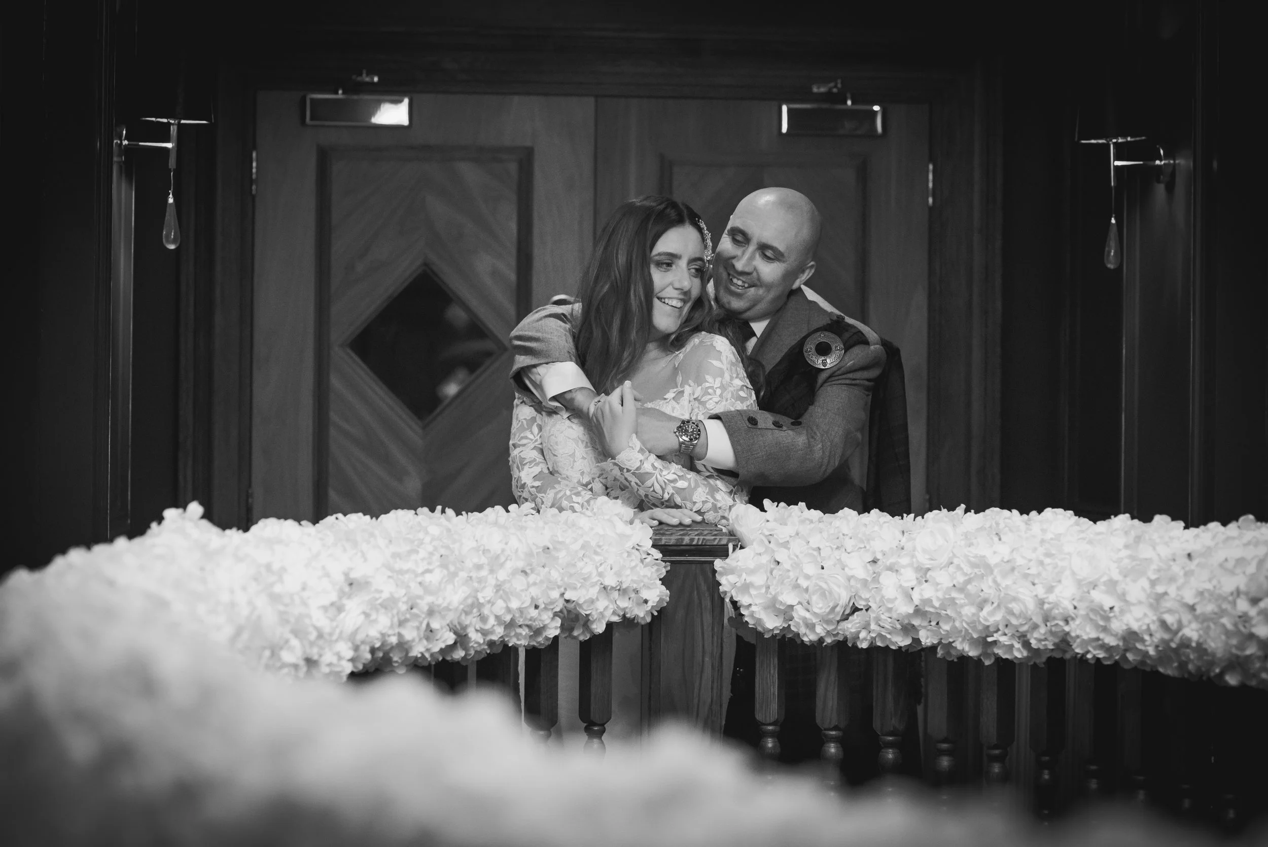 Newlywed couple laughing together behind wedding flowers