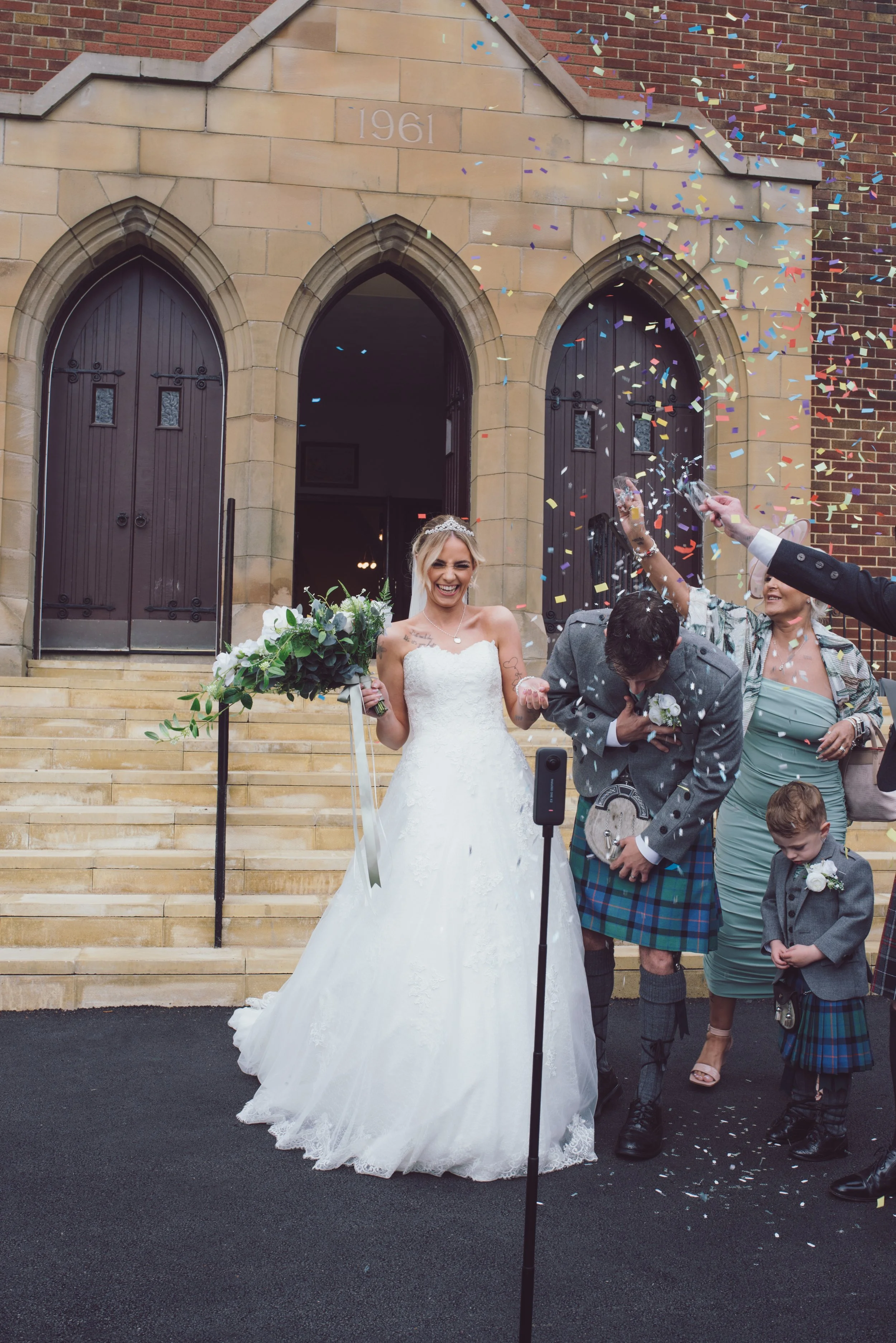 Newlywed couple celebrating outside the church surrounded by confetti and family