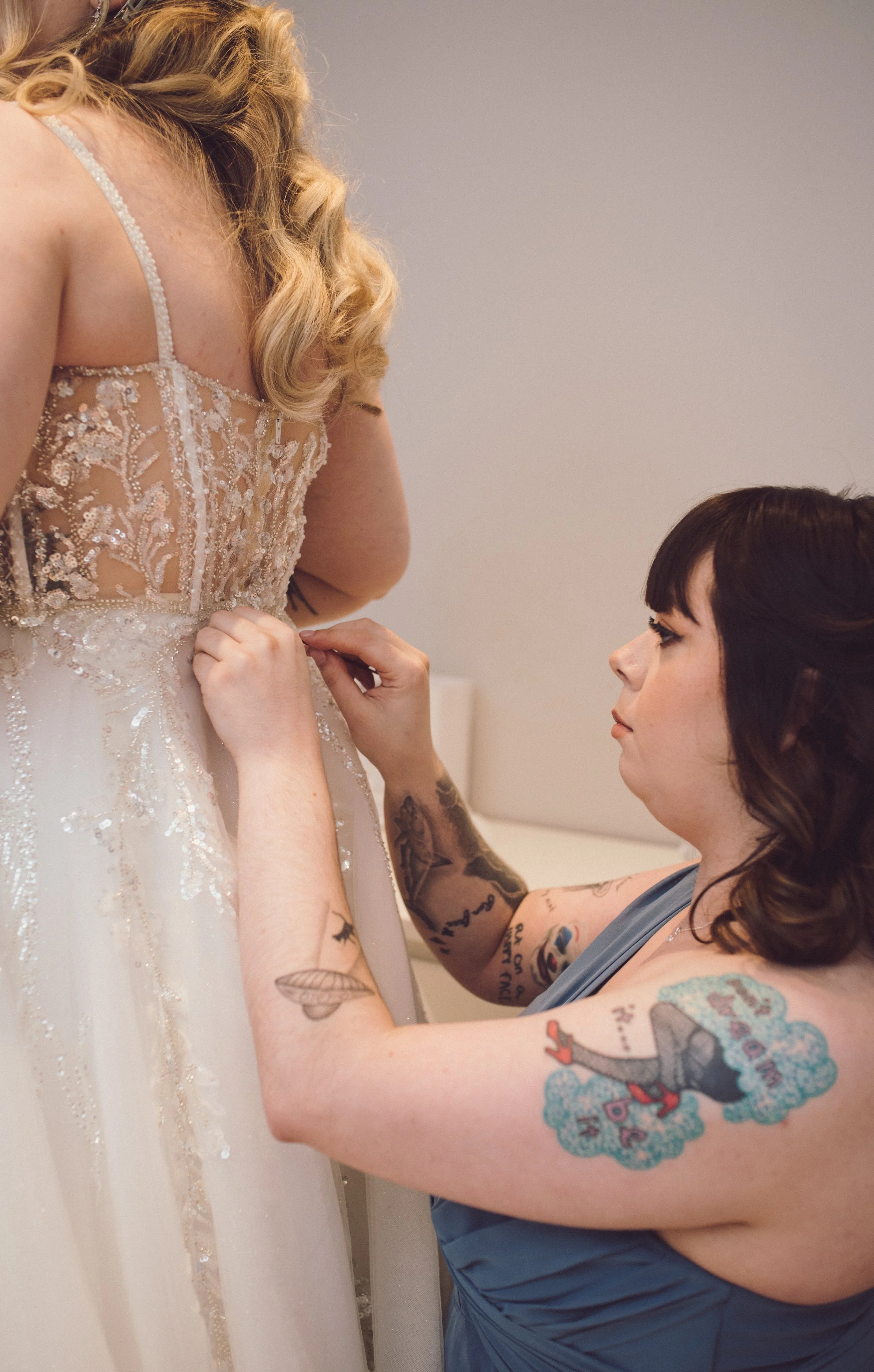 Bridesmaid helping the bride button her wedding dress during preparations