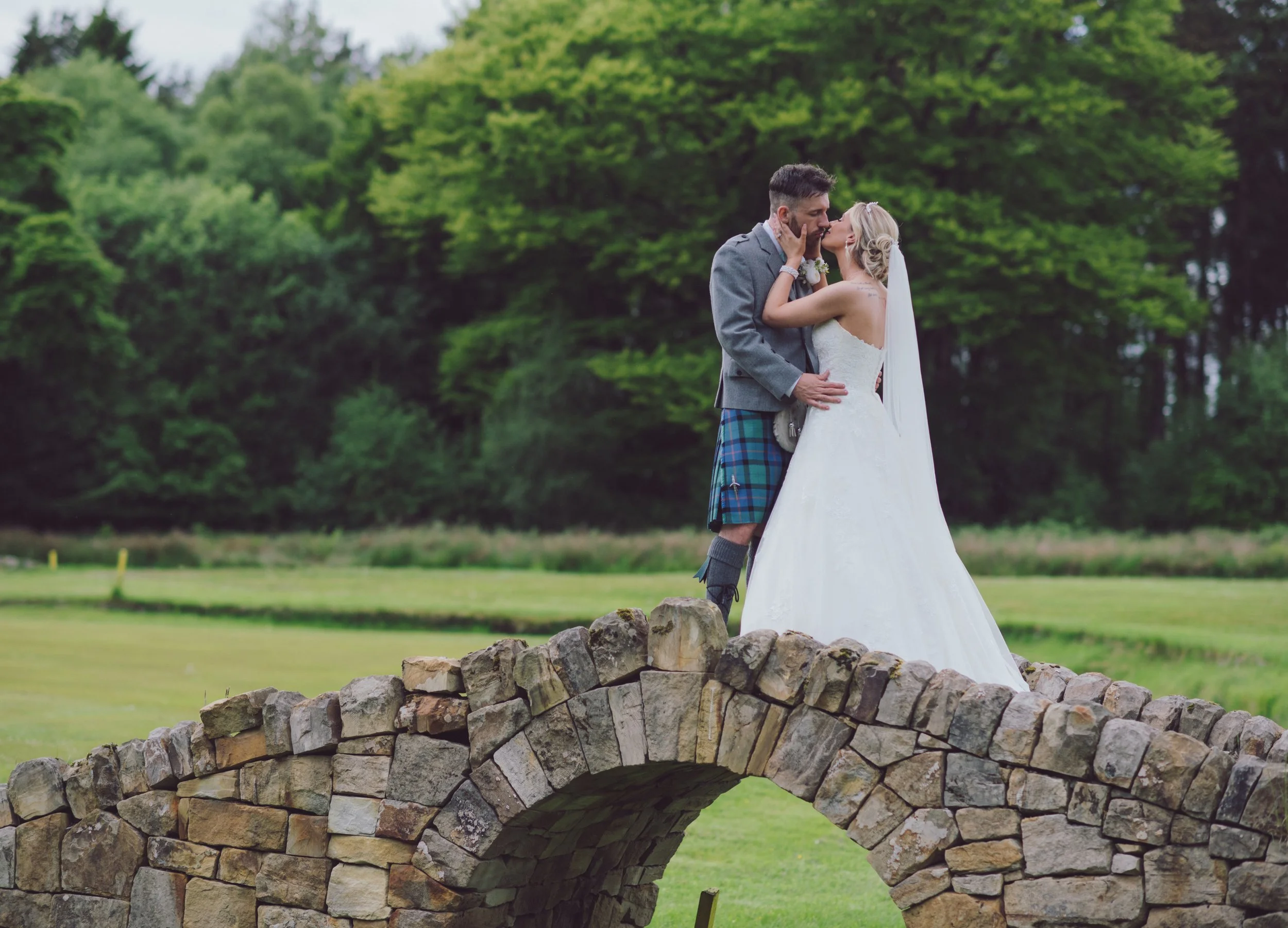 Newlywed couple sharing a romantic kiss on a stone bridge at their wedding venue