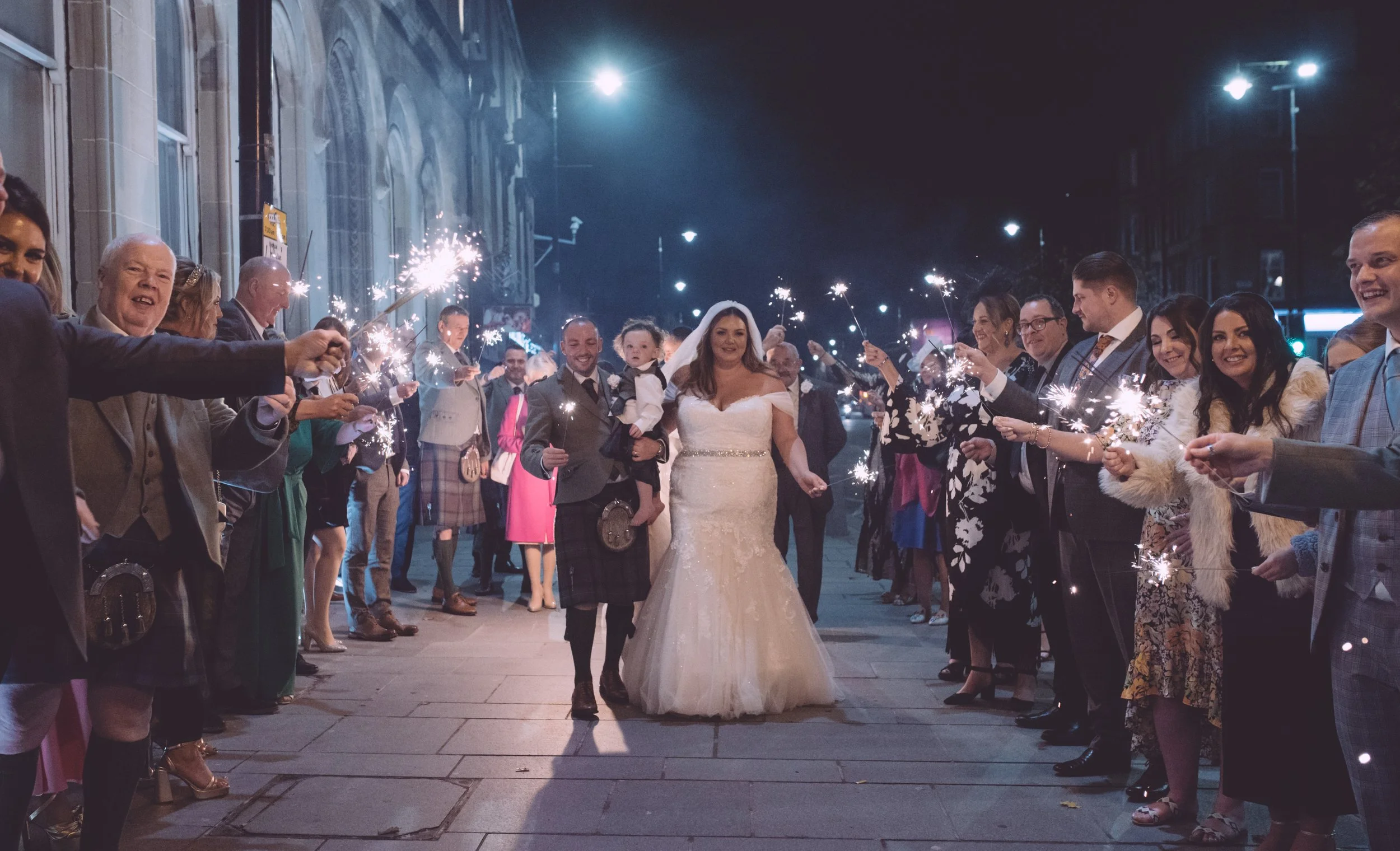 Bride walking through Glasgow at night surrounded by guests holding sparklers