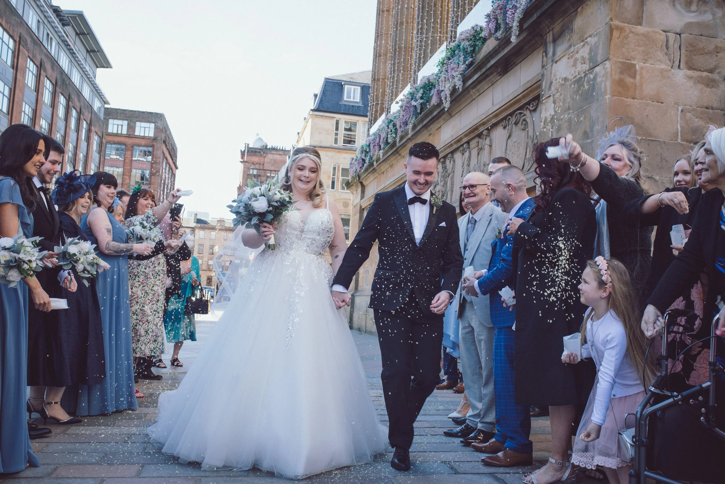 Bride and groom walking through confetti surrounded by wedding guests