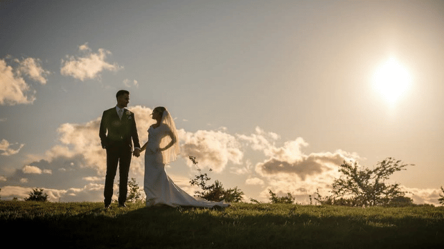 A couple dressed formally holds hands, with the focus on their joined hands and blurred background.