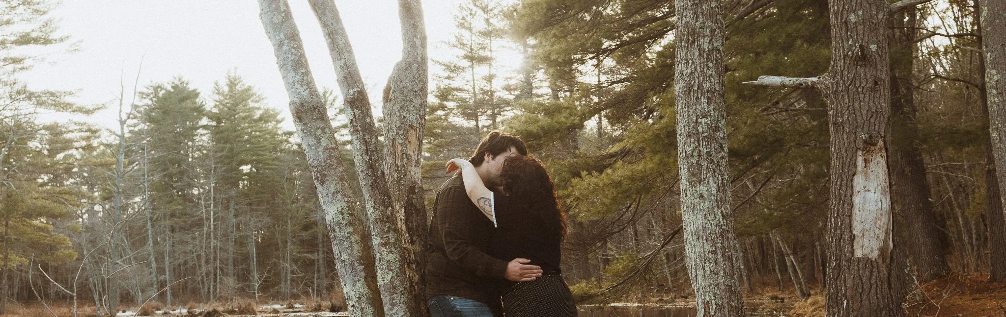 a young couple kisses while the sun sets behind them at Foster Pond Trail in Windham, NH