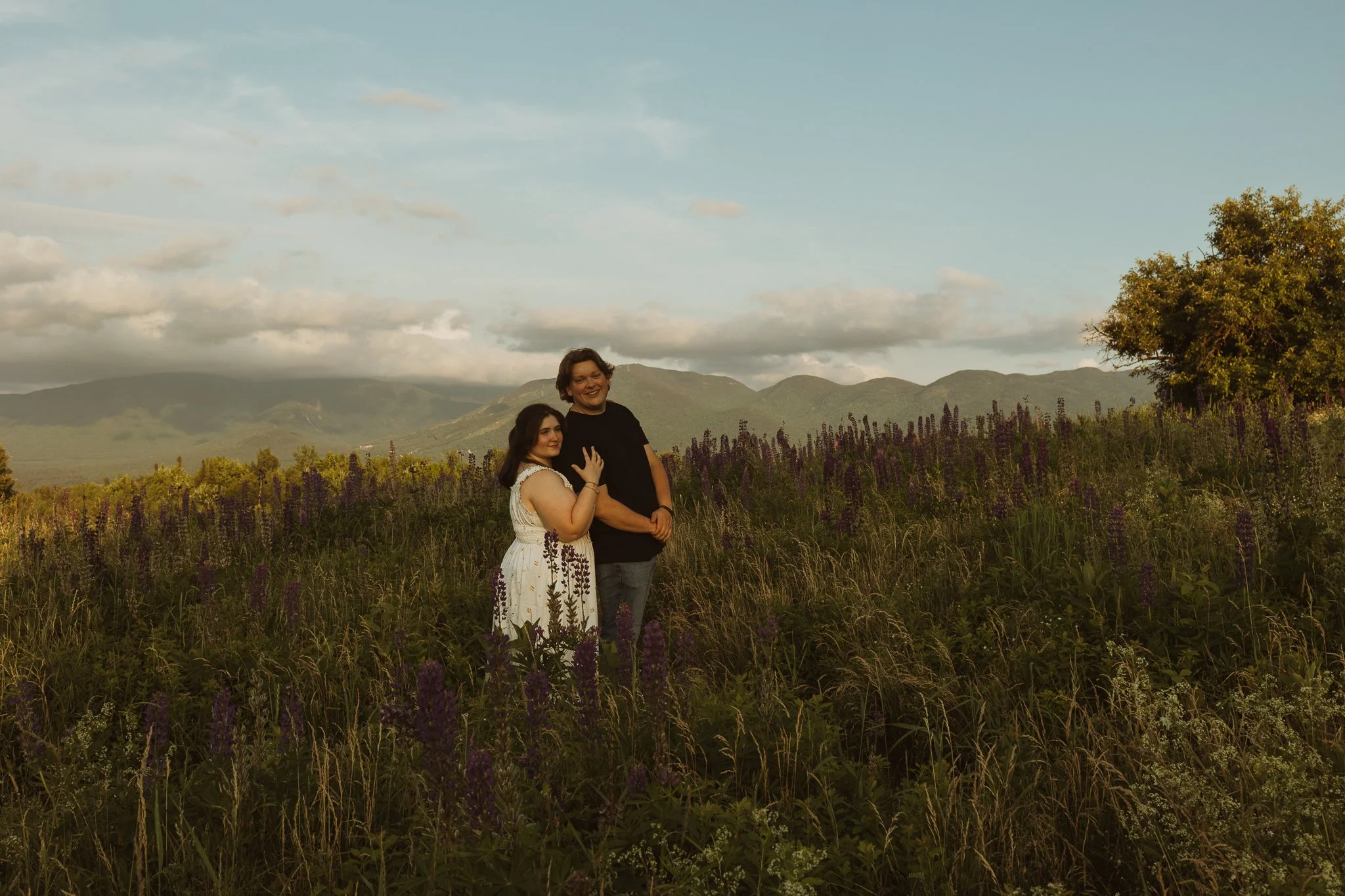 Documentary-style White Mountains elopement photography capturing an adventurous couple in lupine field with mountain ridgeline in the background