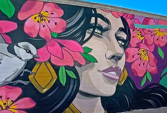 Colorful mural of a woman with long black hair, surrounded by pink flowers and a bird.