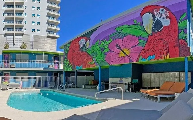 Swimming pool area with colorful mural of two parrots and large pink hibiscus flower on the building wall