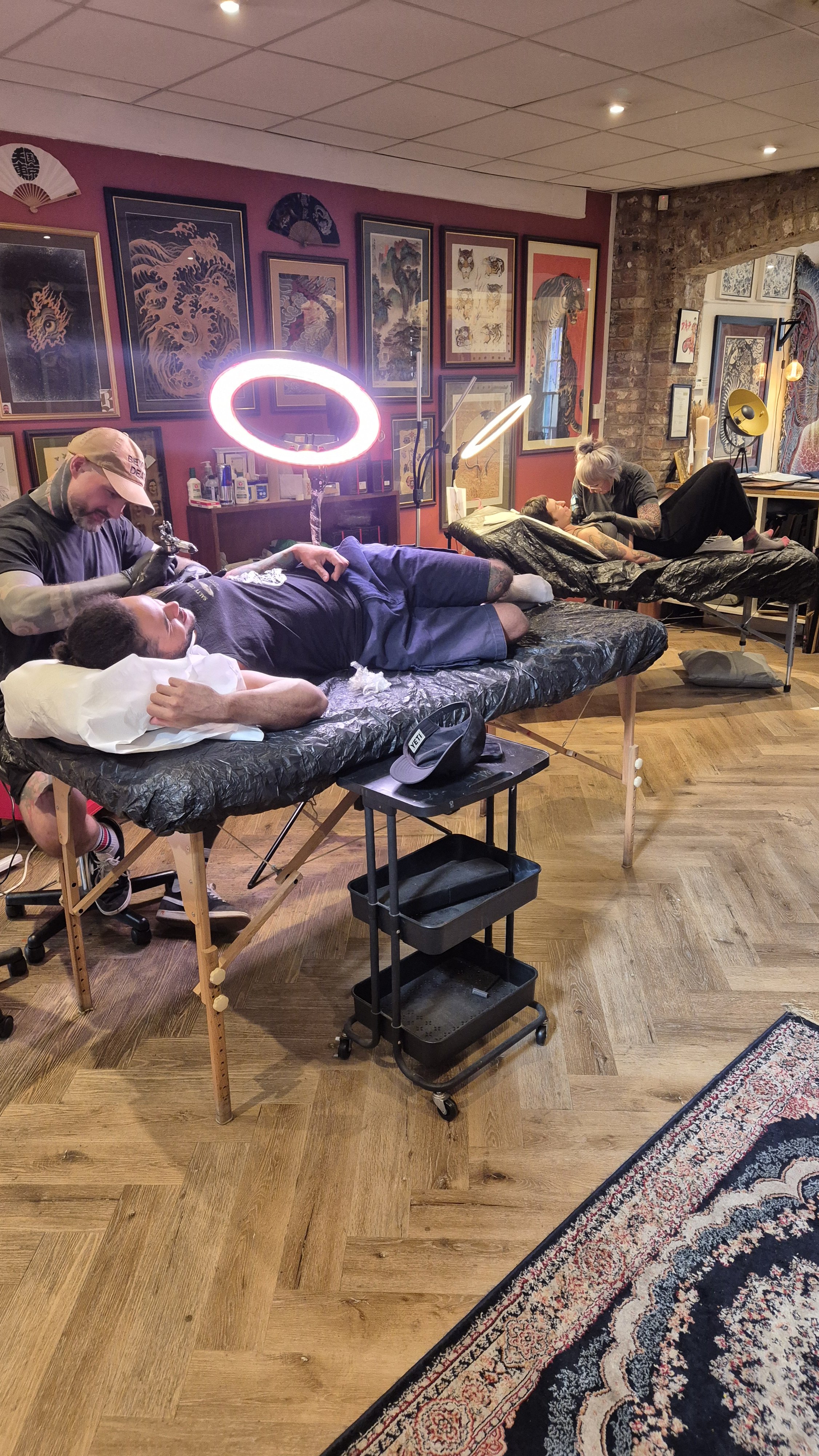 Tattoo artists working on clients in an art-filled tattoo studio.