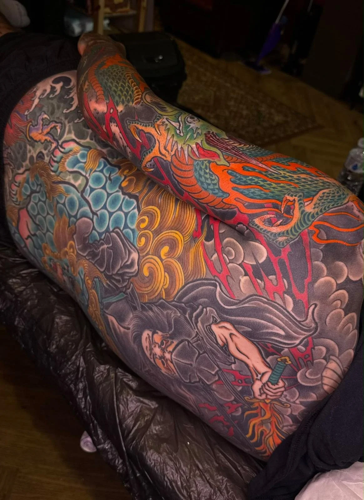 Colorful tattoo sleeve featuring a dragon, clouds, and waves on a person's arm.
