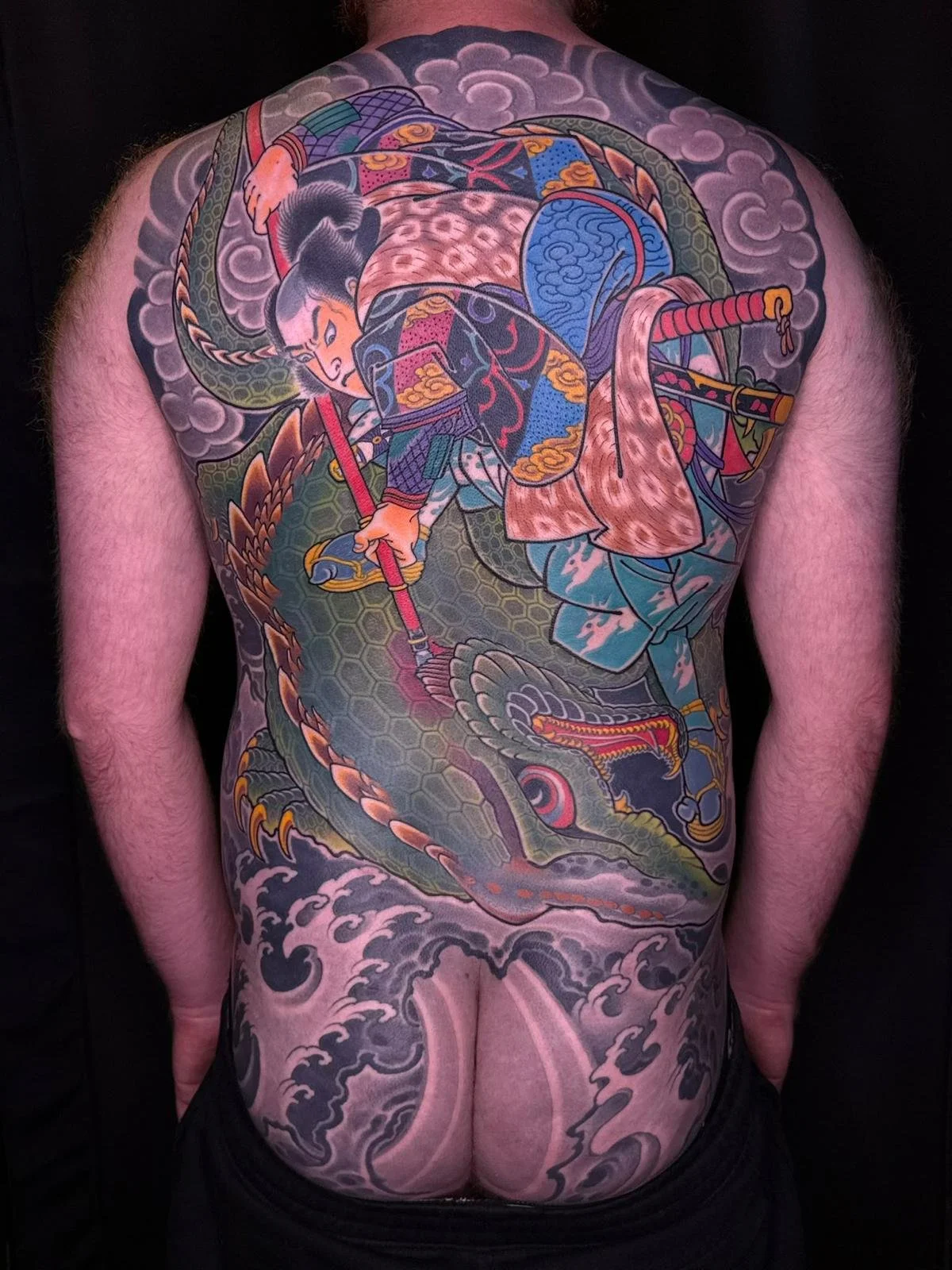 Colorful Japanese-style tattoo of a warrior fighting a dragon covering a man's back and buttocks.