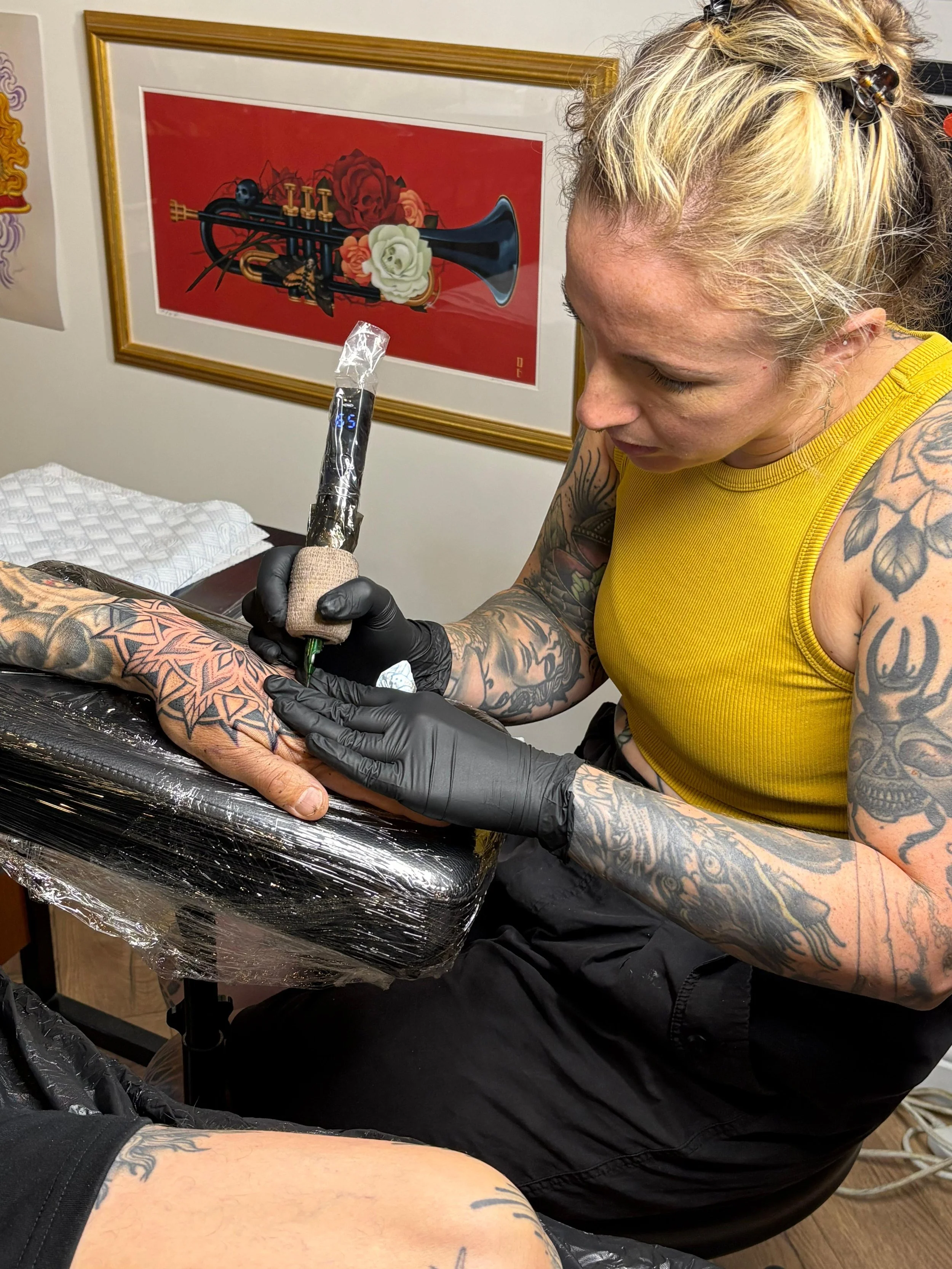 A woman with tattoos getting a tattoo on her arm in a tattoo studio.