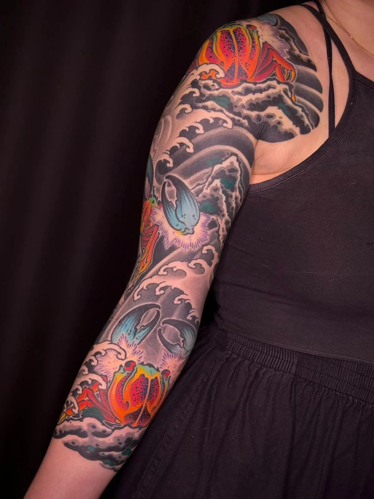 Tattoo sleeve featuring waves, a whale, and colorful designs on a person's arm.