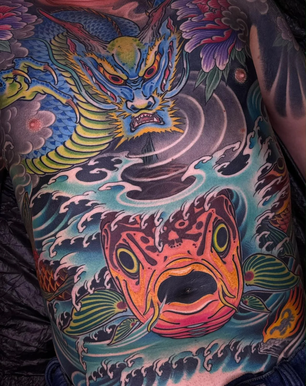 Colorful Japanese-style tattoo of a fierce dragon and tiger on a person's back, with waves and clouds.