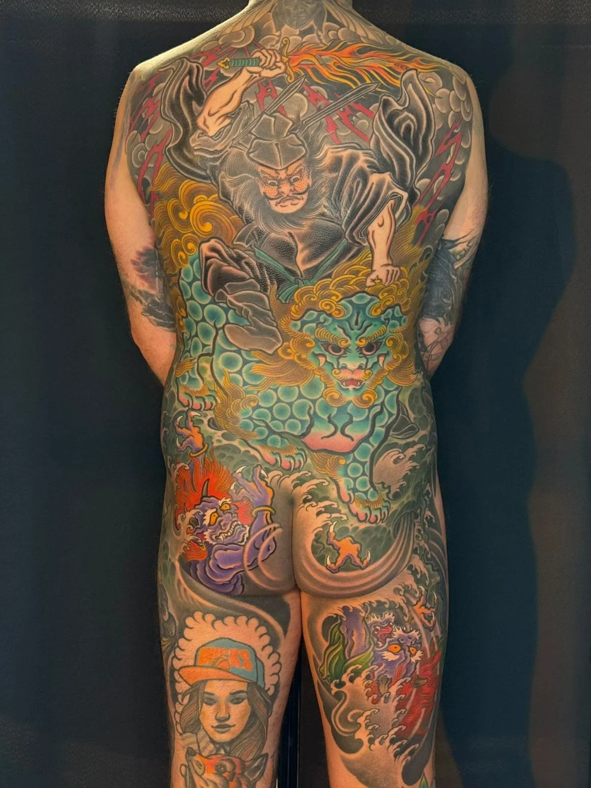 Full back tattoo depicting a samurai warrior, a fierce lion head, and various traditional Japanese motifs in vibrant colors.