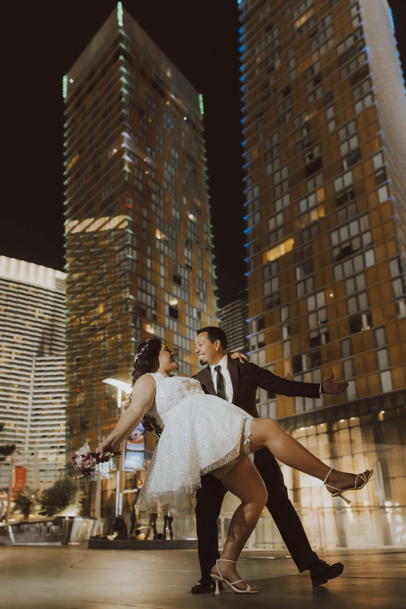 A couple dancing in a city square at night, surrounded by tall modern buildings with illuminated windows.