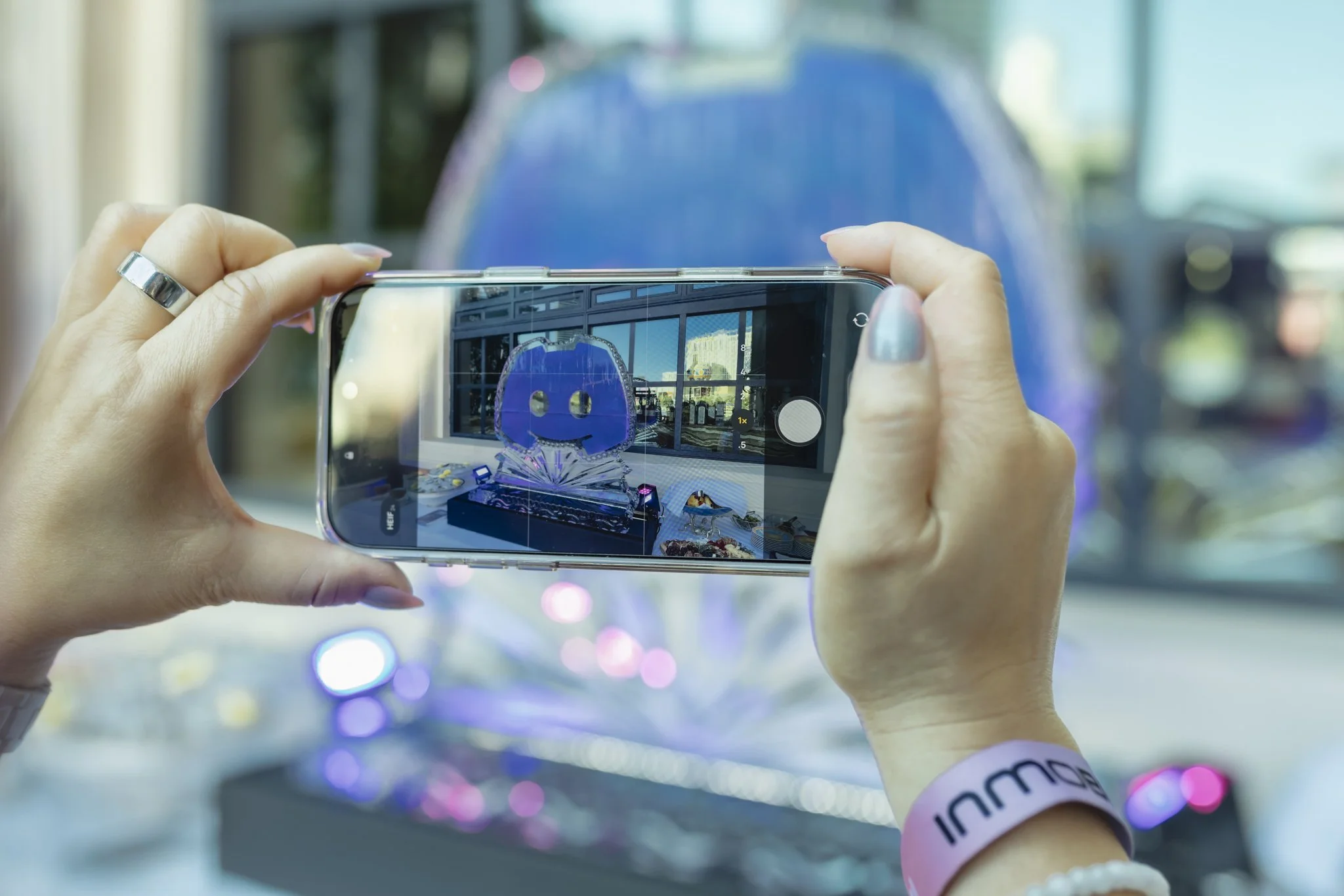 Person taking a photo of a store window display with a smartphone, showing a blue figure with a smiling face in the reflection.