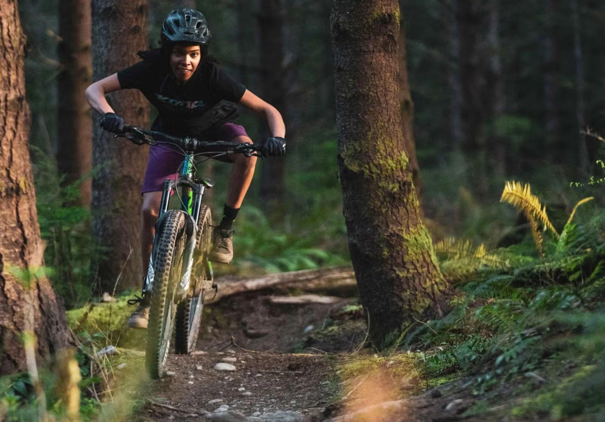 Woman mountain biking through a forest with helmet and dark bike clothes