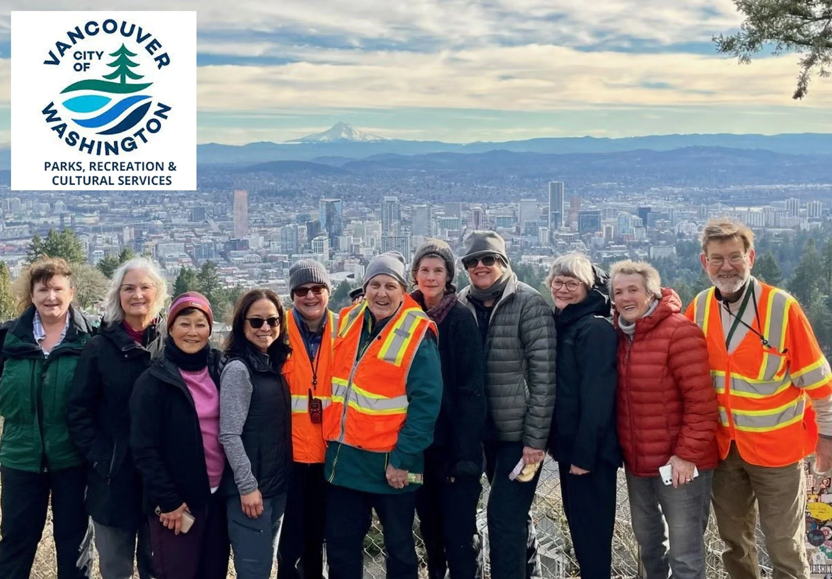 A group of senior citizens stand at a lookout in Portland, Oregon with a view of the City and Mt. Hood in the background and the City of Vancouver logo