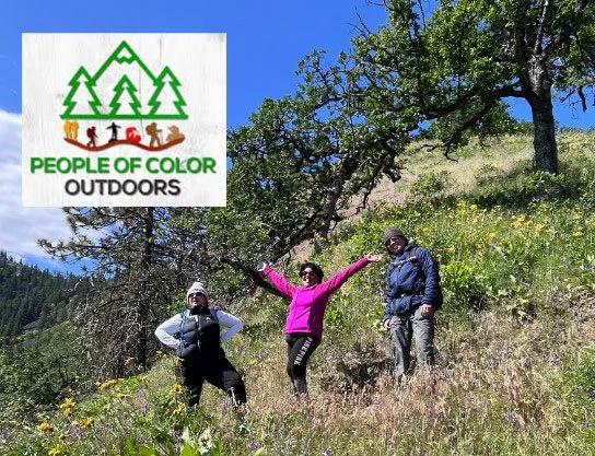 Three people hiking on a hill side with mountain flowers and trees in the background, with the People of Color Outdoors logo