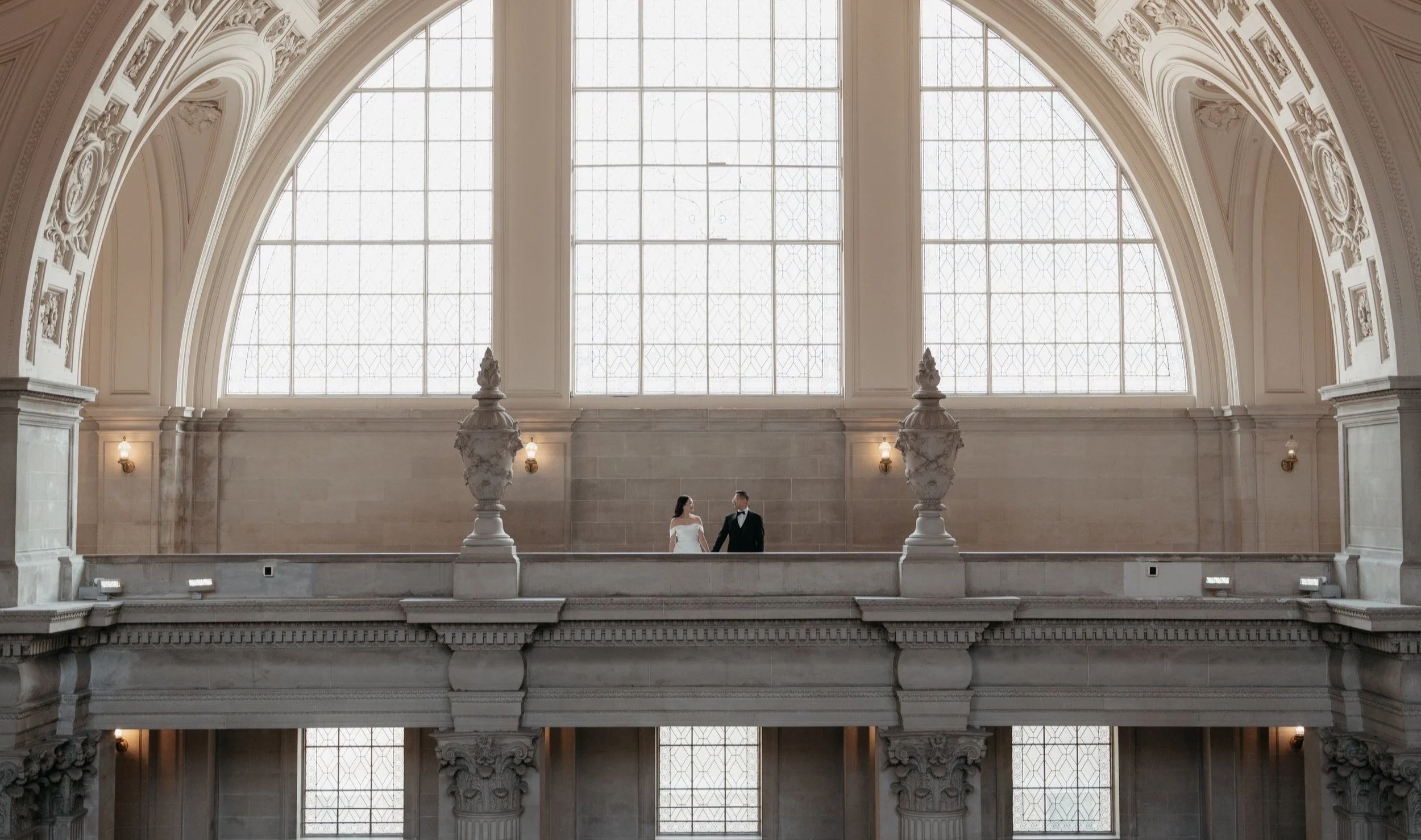 Wedding couple walking beneath grand arched windows