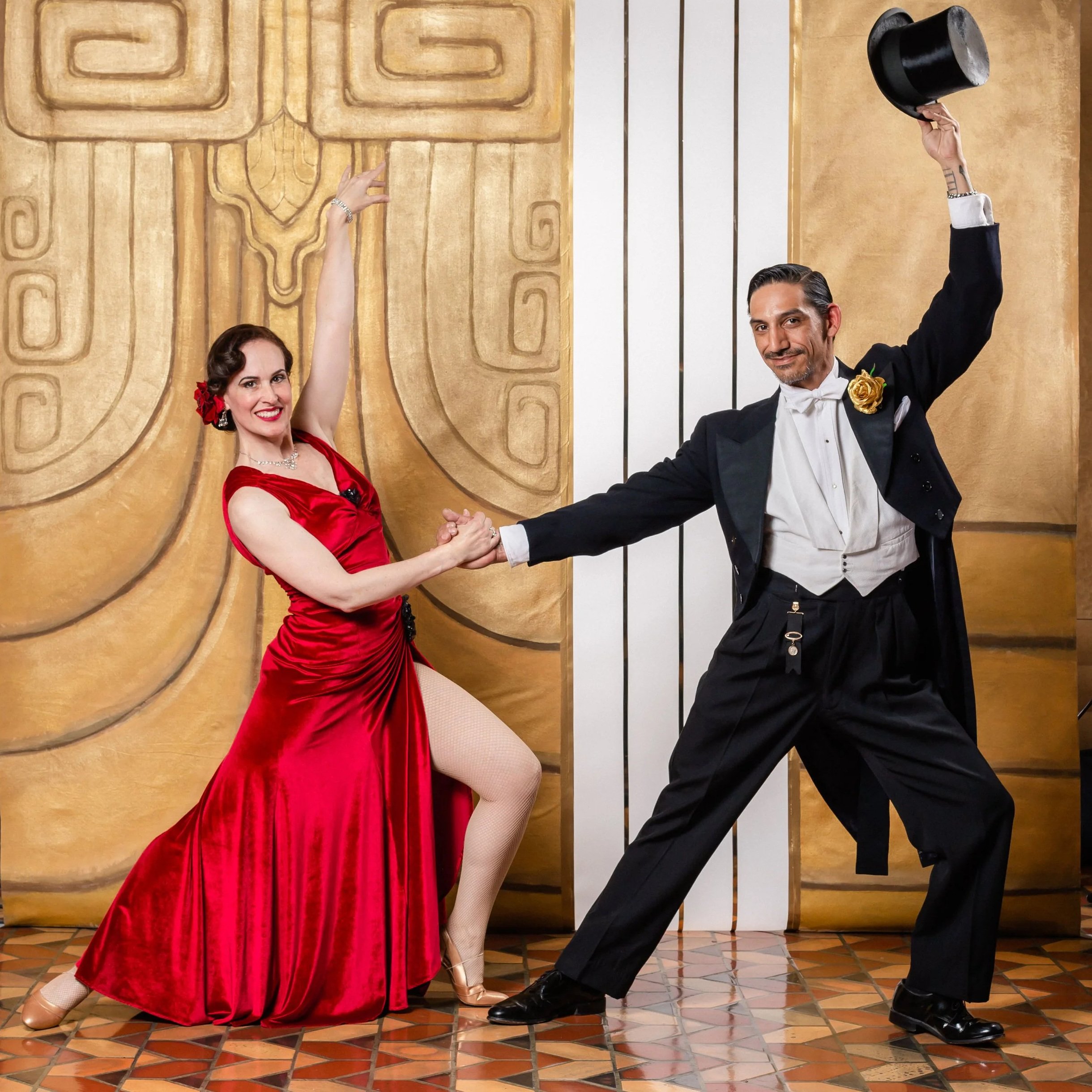 A man in a white shirt and black pants dancing with a woman in a sred dress and gold shoes.