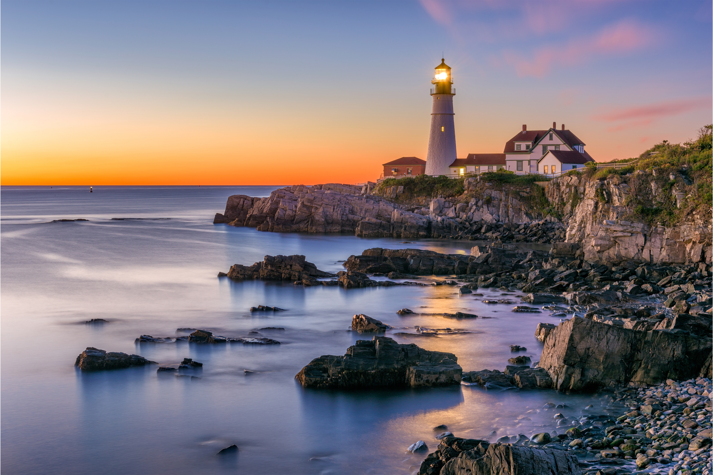 Lighthouse on a rocky coast at sunset with colorful sky and calm water