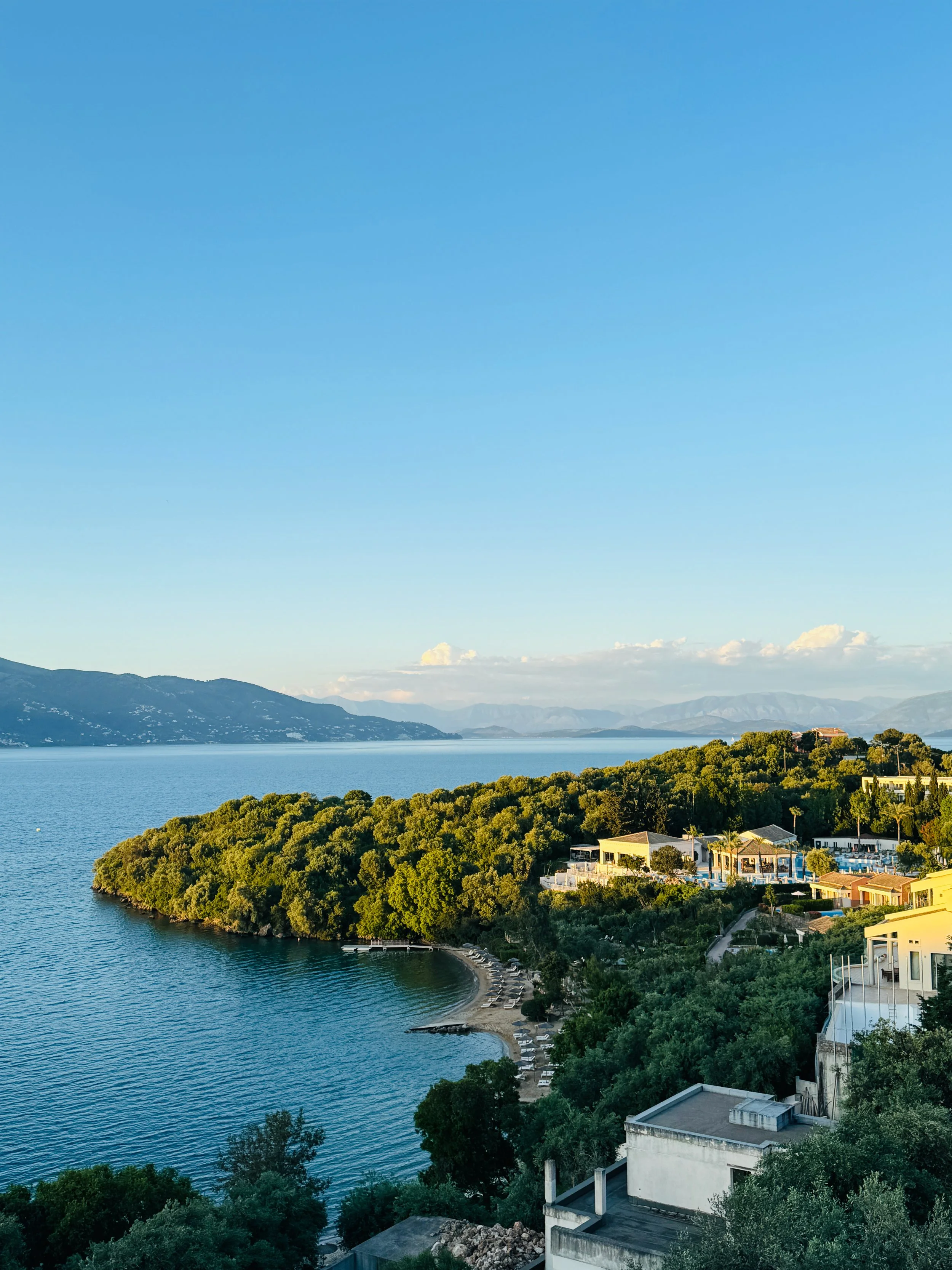 Vue d'une côte avec des bâtiments modernes, une plage et des arbres, sous un ciel bleu clair