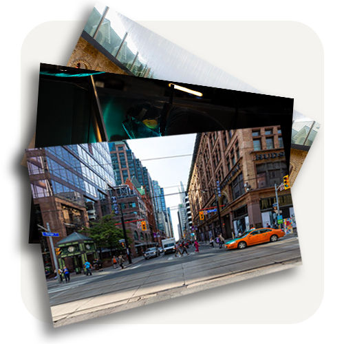 Une rue urbaine avec des bâtiments modernes, des piétons, une voiture orange et des feux de circulation.