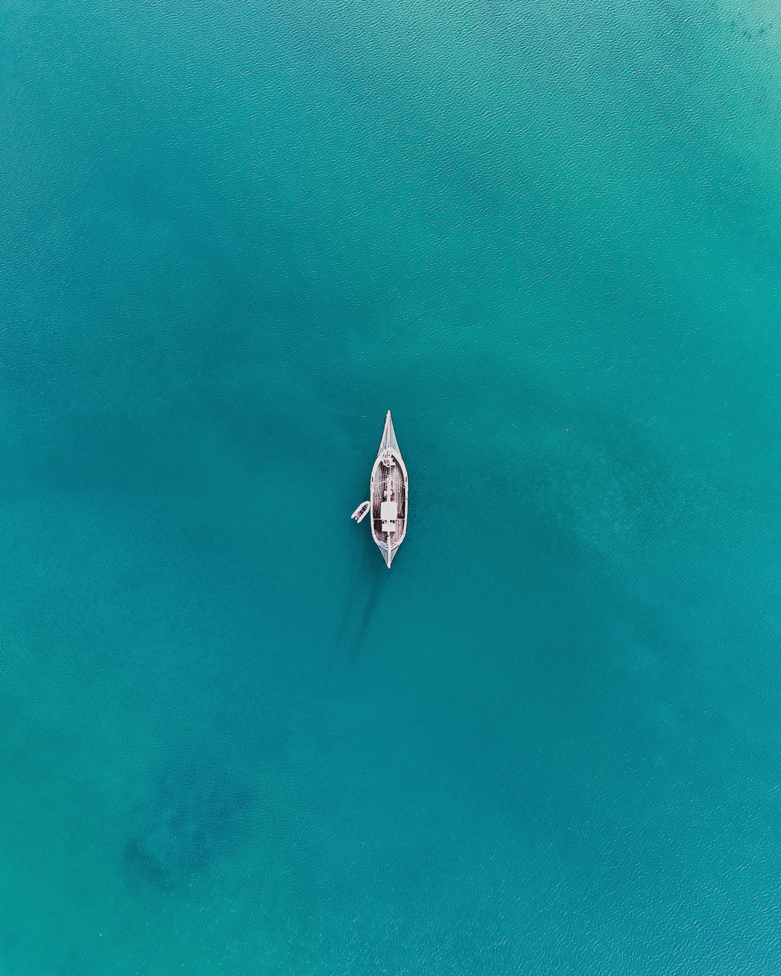Vue aérienne d'un bateau à voile blanc sur une mer turquoise calme.