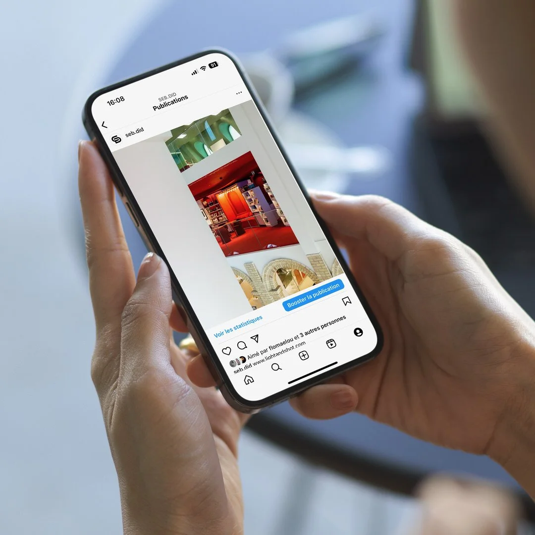Une personne tenant un téléphone intelligent affichant une publication Instagram avec plusieurs images colorées, dont une bibliothèque ou une salle d'exposition intérieure.