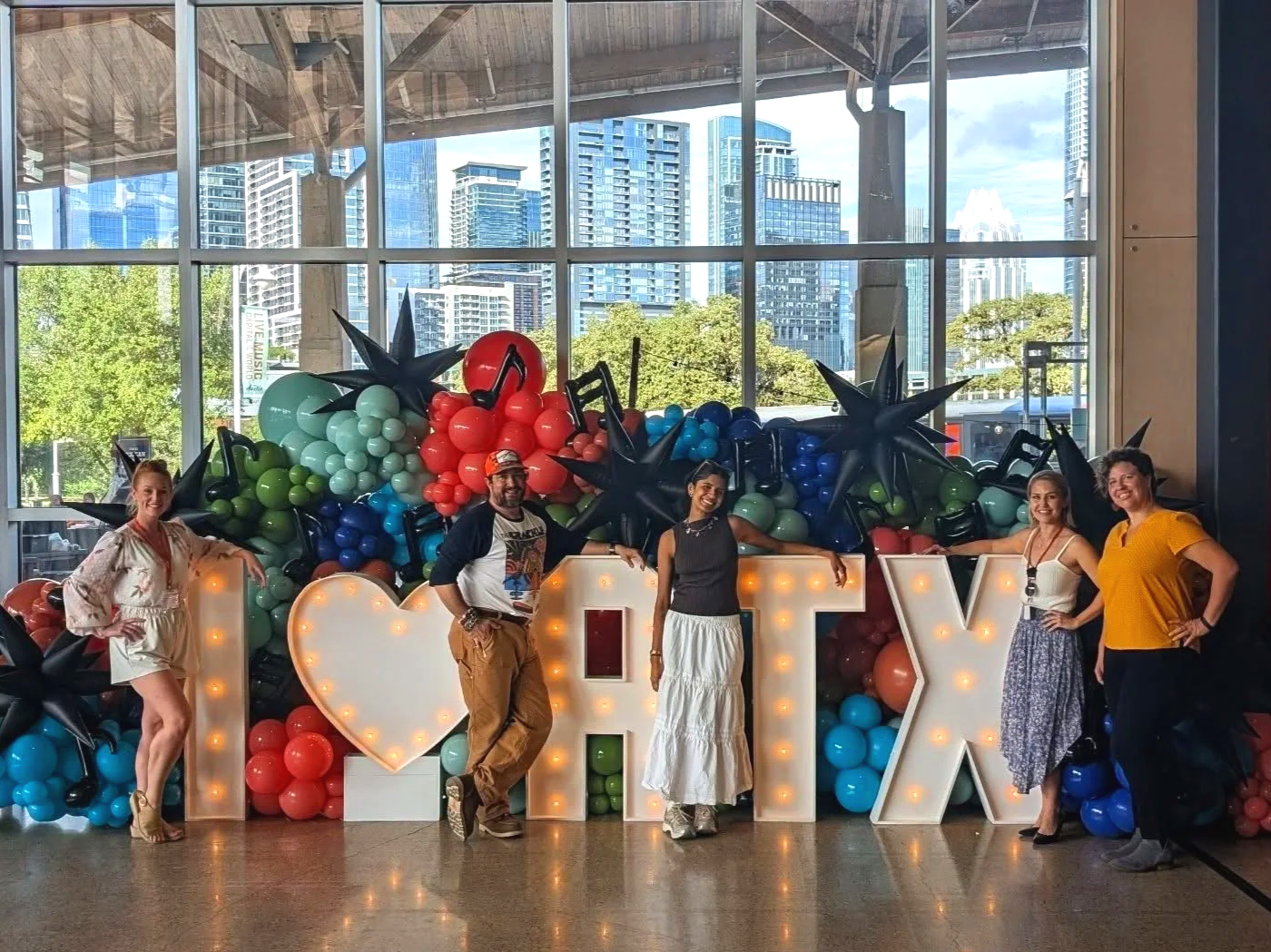 Local people standing around a Stunning custom organic balloon garland around marquee lights saying I love Austin in front of the city skyline with music note balloons and black stars