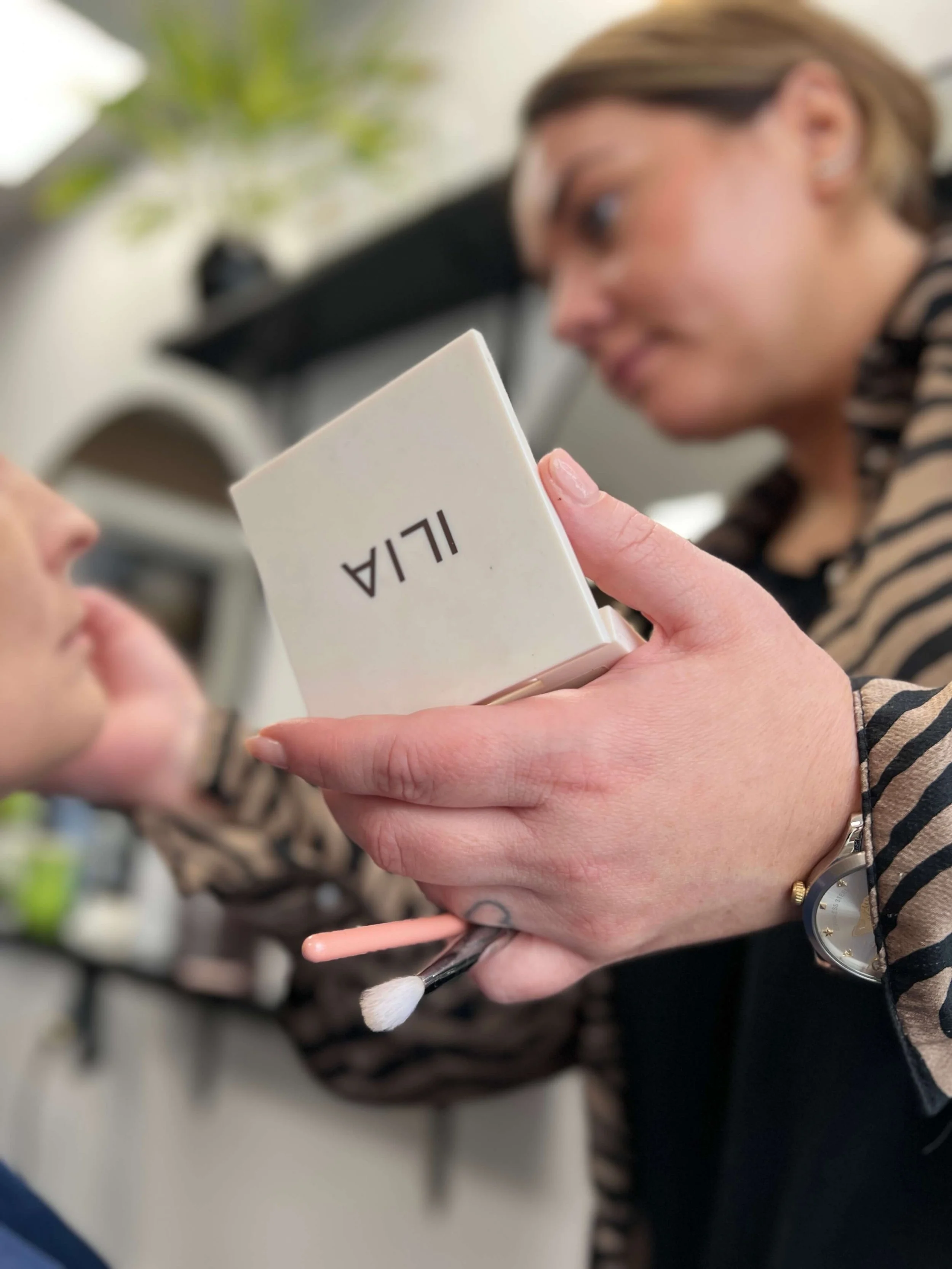 Makeupartist arbejder koncentreret med palet og pensler under brudestyling, fokus på hænder og detaljer