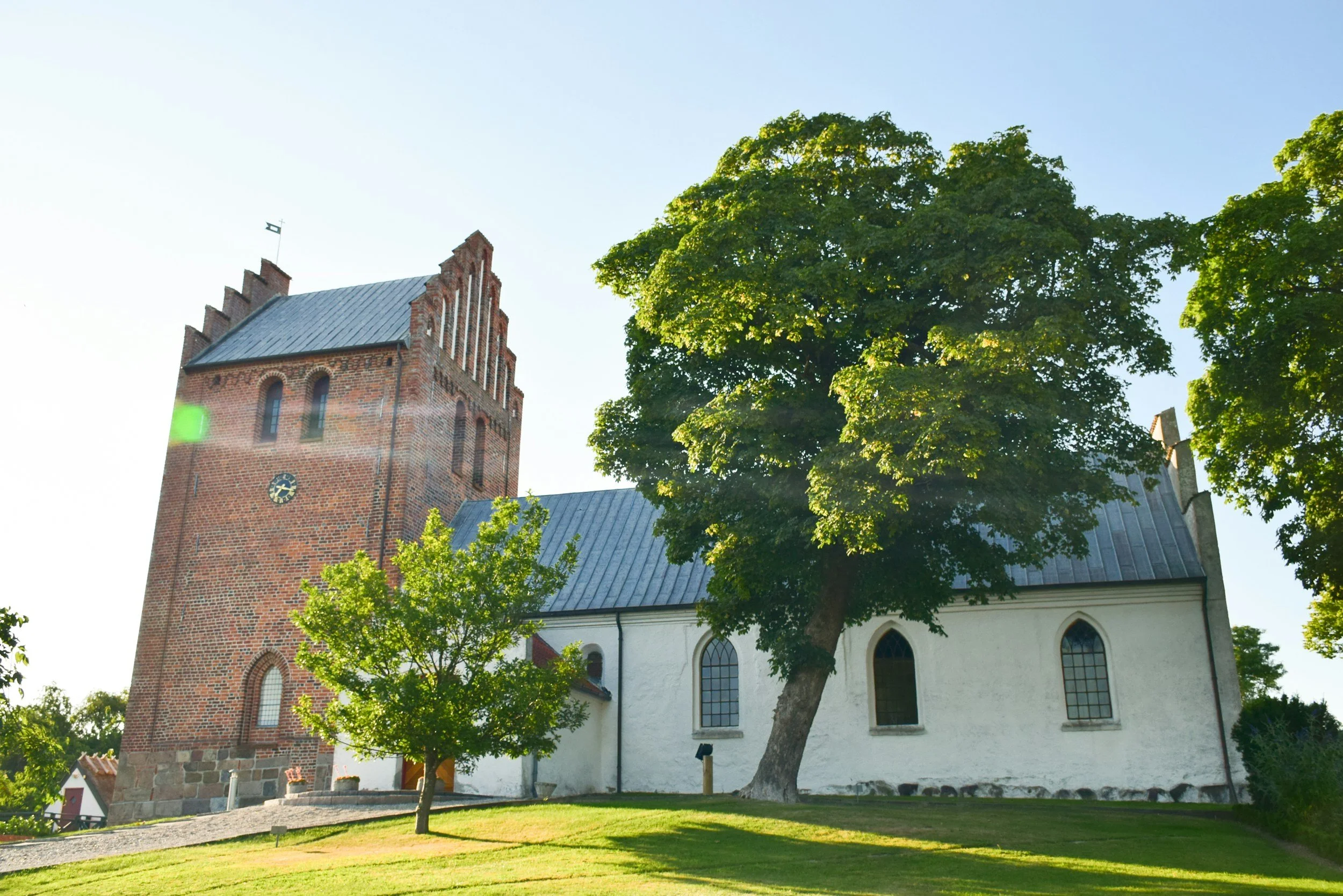 Dansk kirke i solskin og med træer til at give skygge