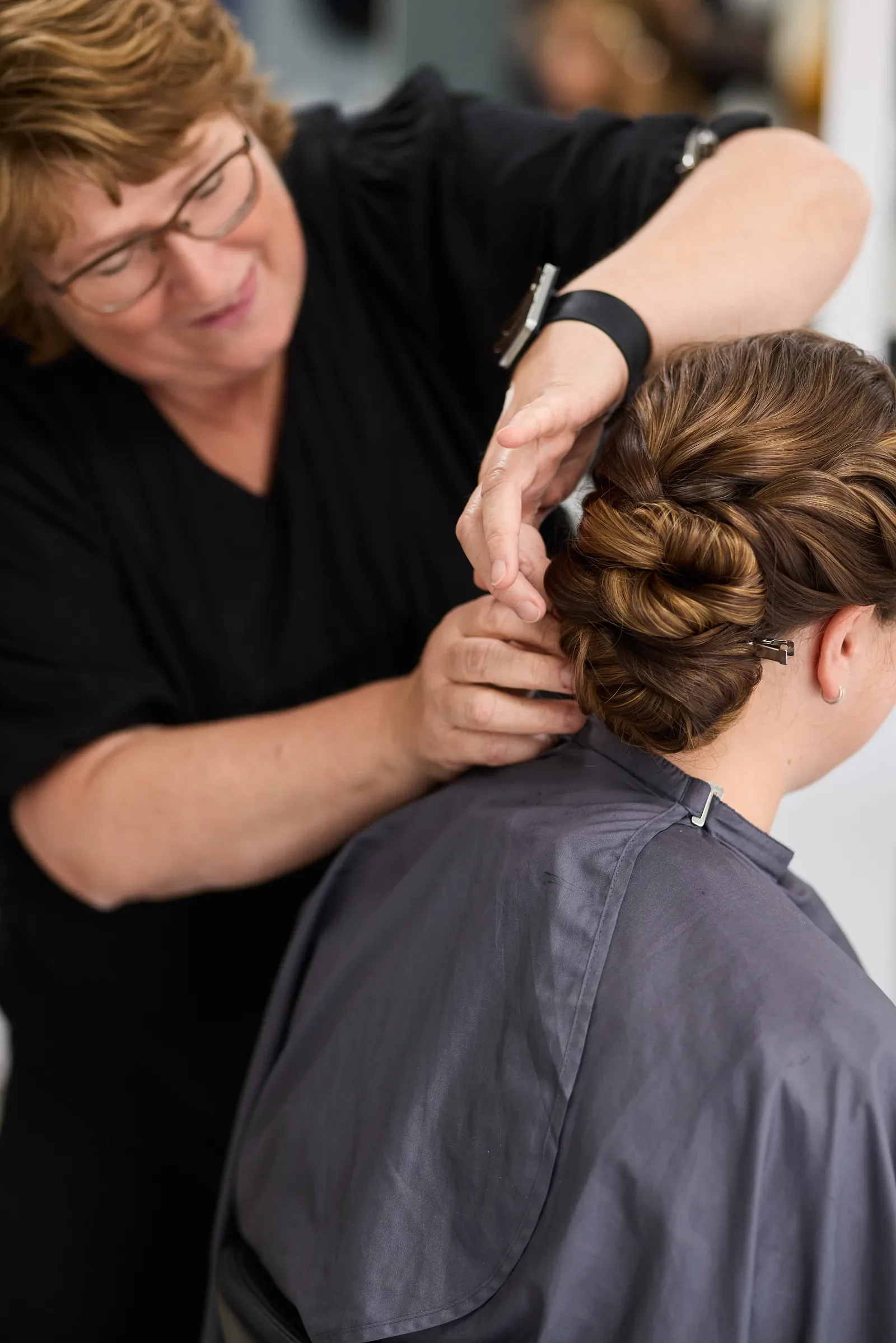 smuk brudeopsætning i kraftigt mørkt hår frisøren koncentrerer sig om at sætte håret godt fast så det ikke falder ned